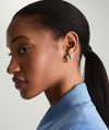 A woman with a ponytail wearing Plush Small Hoops, handcrafted 14k gold earrings, highlighting their pillowy design on her lobes.