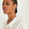 Woman wearing Bold Pearl Drop Earrings, featuring freshwater pearls and handcrafted in 18k gold vermeil, paired with a white shirt and gold chain necklace.