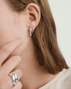 Close-up of a woman's ear wearing the Ella Double Hoop, featuring a simple hoop paired with a striking lab-grown sapphire hoop in various gemstone cuts.