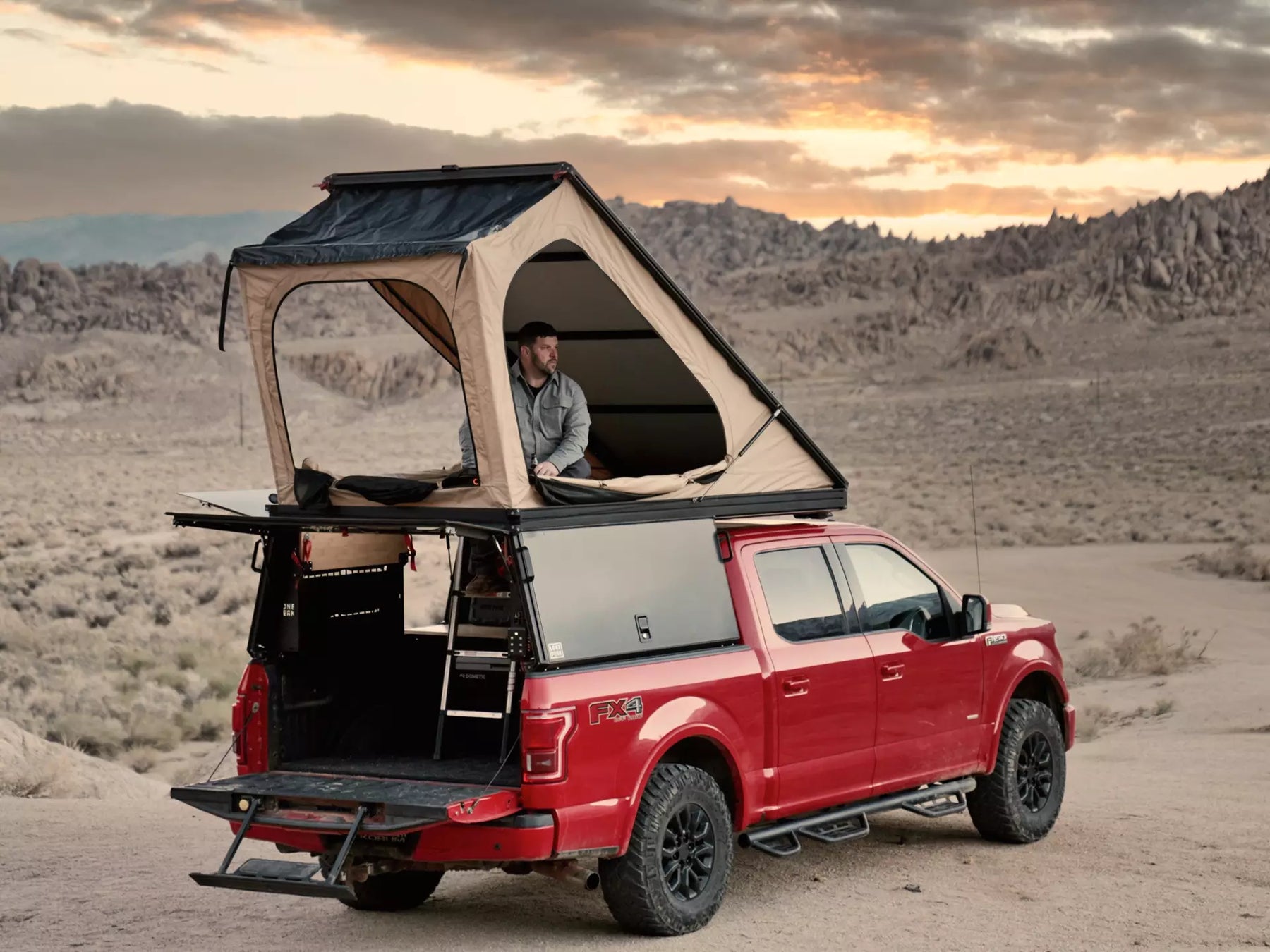 A man sits in a Lone Peak Camper on a truck in the desert
