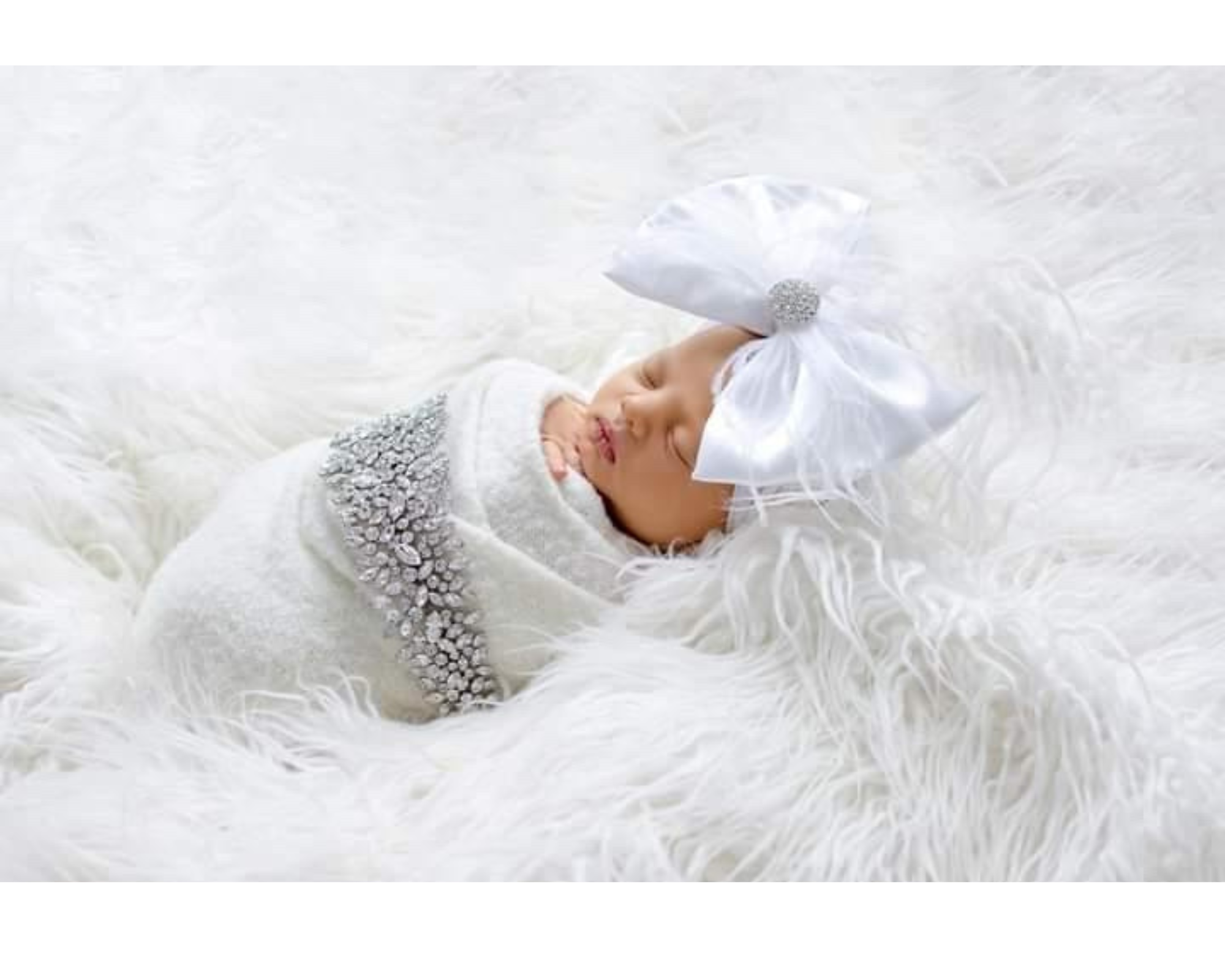 A sweet baby swaddled in white wearing her mommy’s Swarovski crystal bridal headpiece.