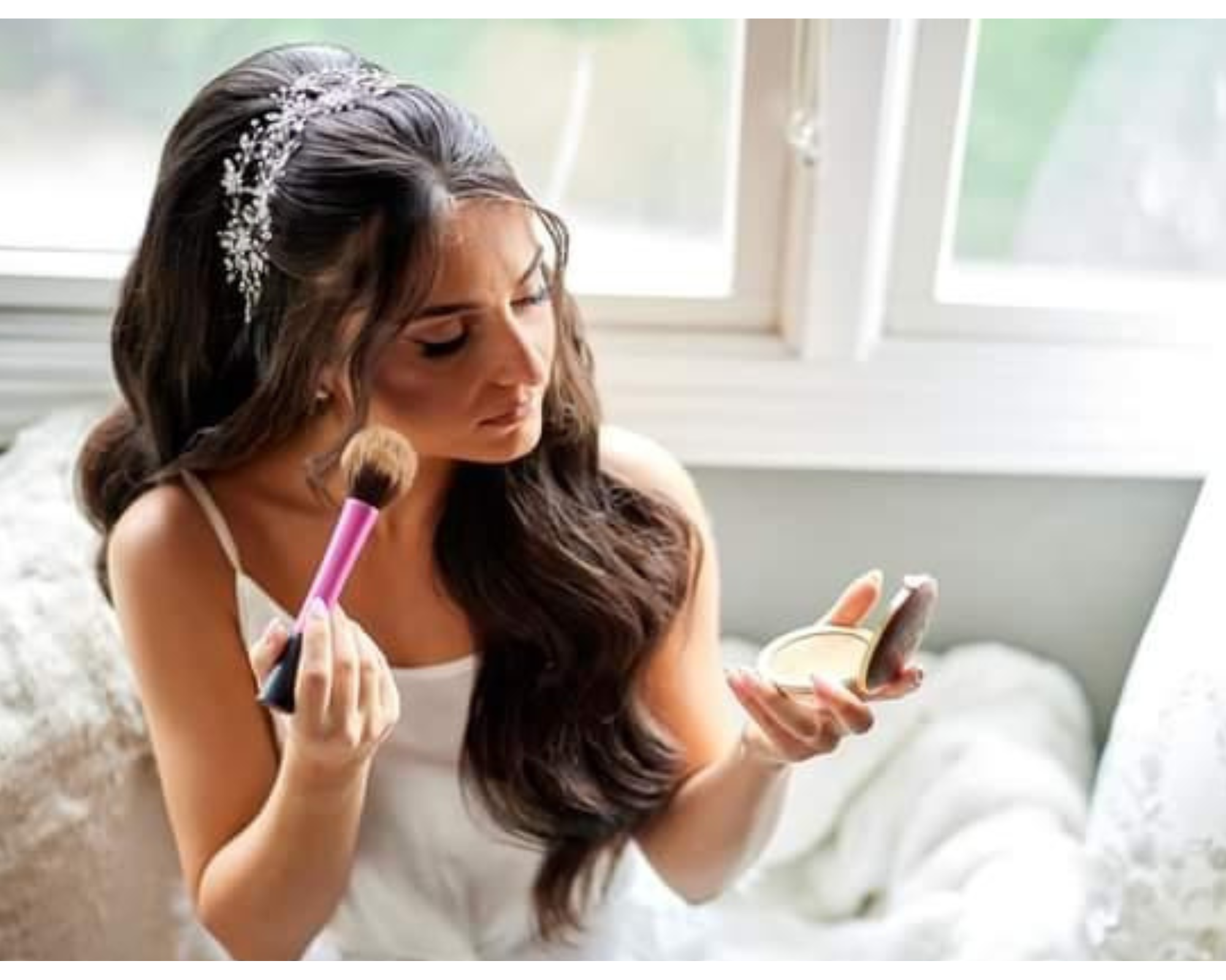 A beautiful bride putting on her makeup while wearing her hair down with a delicate crystal bridal hair vine