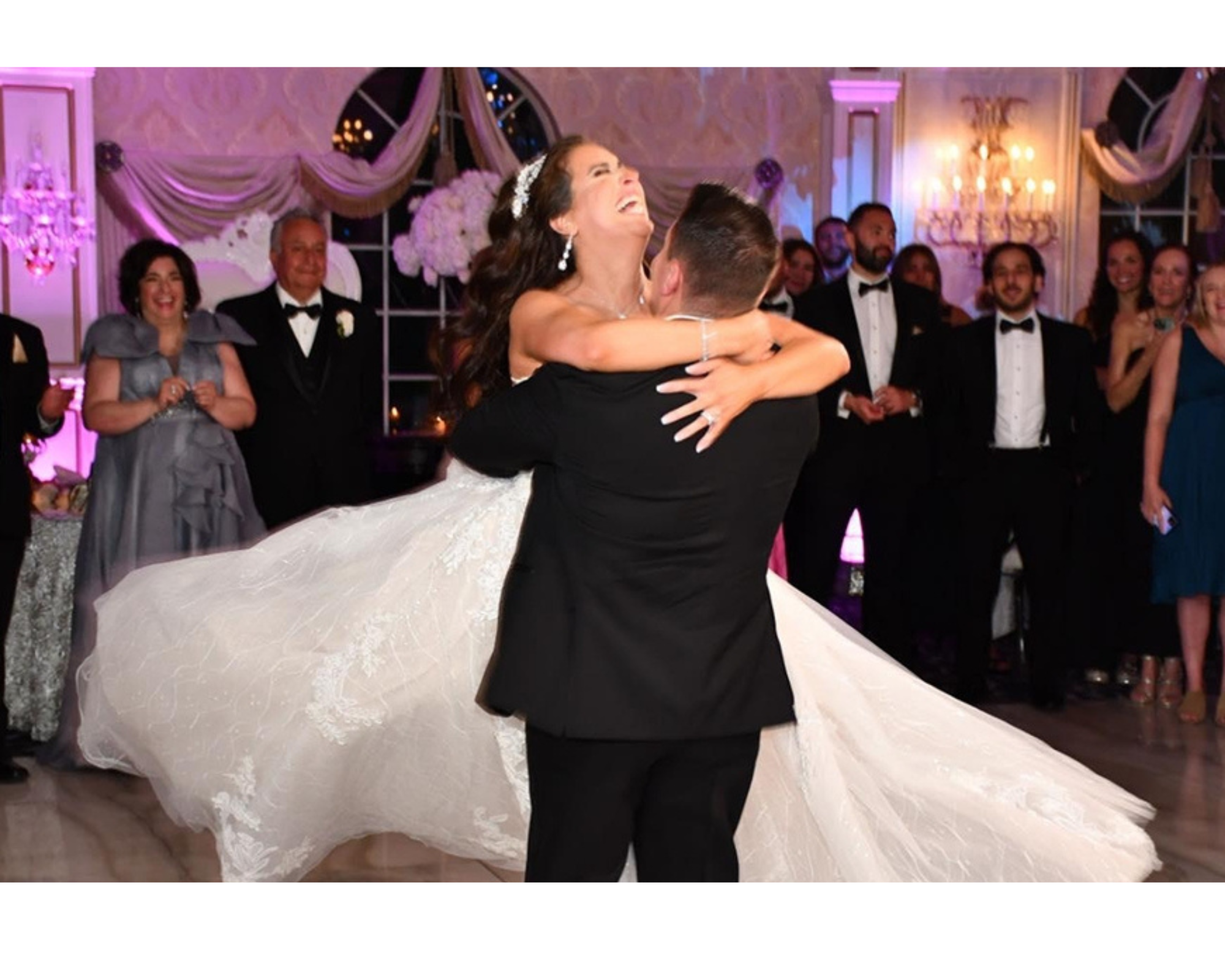 A bride and groom on the dancefloor. He is twirling her in his arms, and she is laughing and joyful.