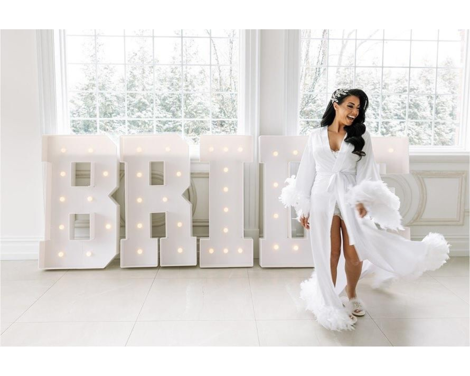 Our beautiful bride dances in front of a giant lit-up sign reading, 'bride.' She's wearing a white robe and her Swarovski crystal hair vine.