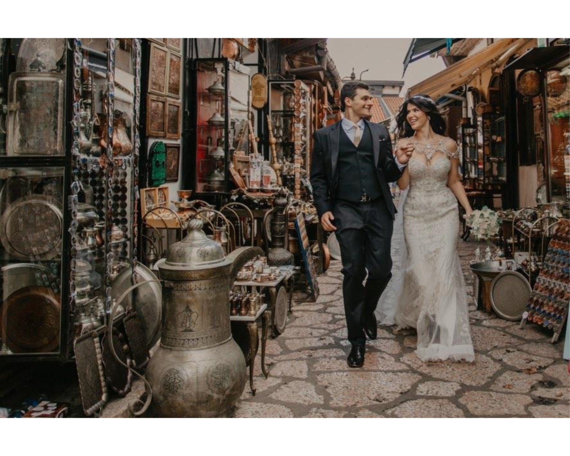 Our bride and groom on a quaint European street. She’s wearing her lace gown, custom wedding dress jewelry, and crystal wedding headpiece.