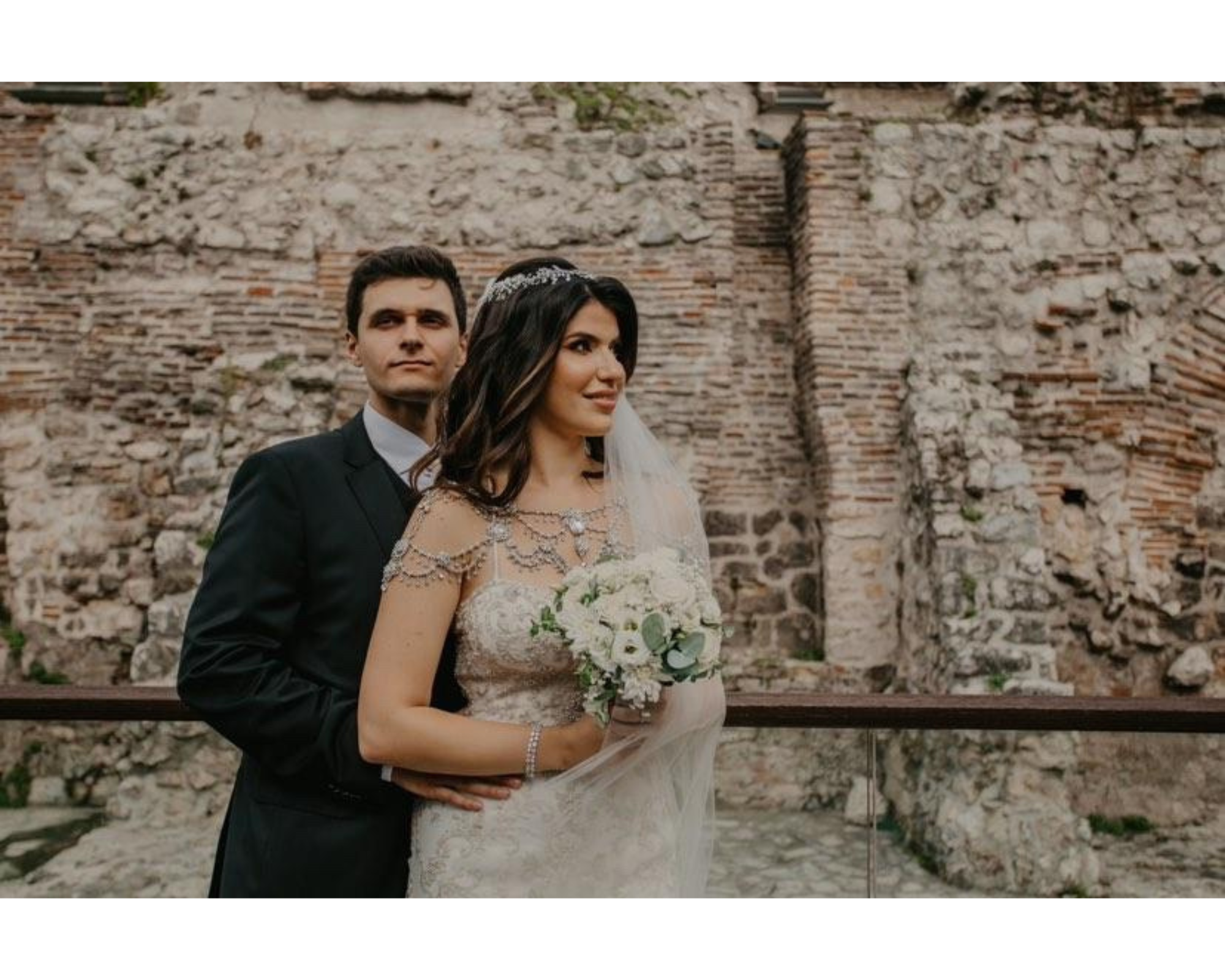 Our bride and groom on a quaint European street. She’s wearing her lace gown, custom wedding dress jewelry, and crystal wedding headpiece.