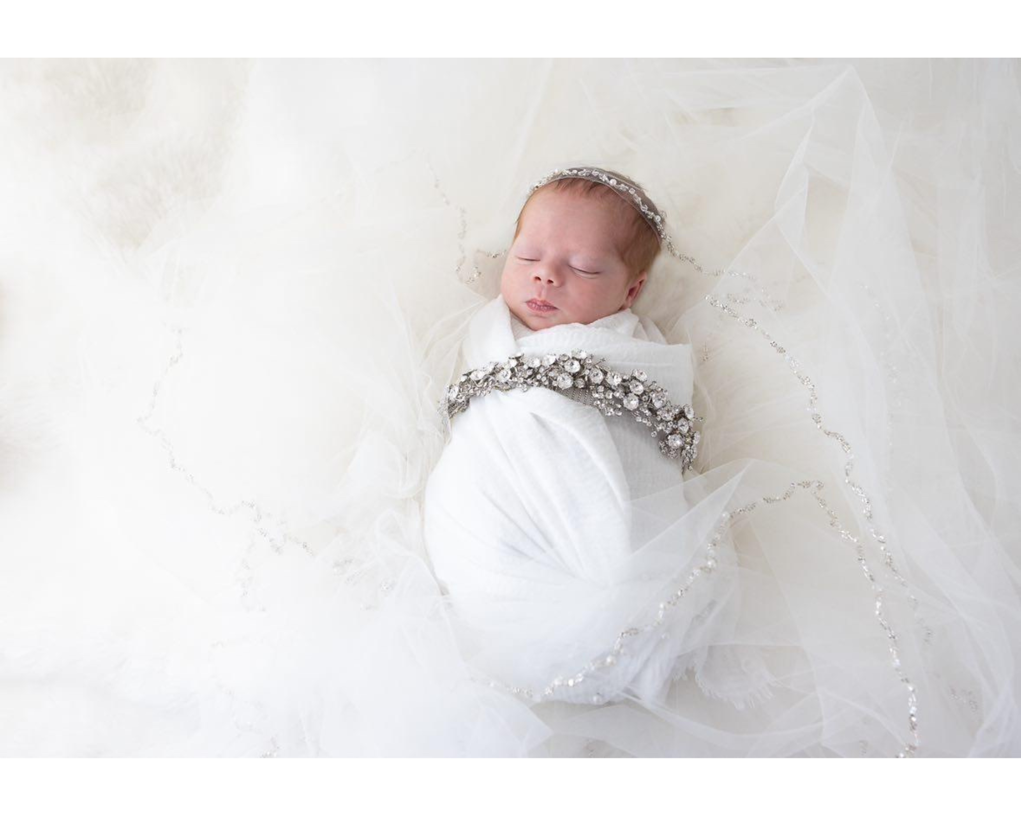A baby wrapped in a white blanket wearing her mom's Swarovski crystal bridal headpiece.