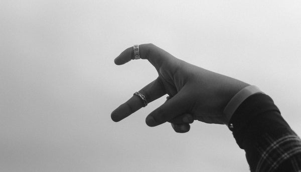 black and white photo of a person's hand wearing minimalist rings making a half heart sign