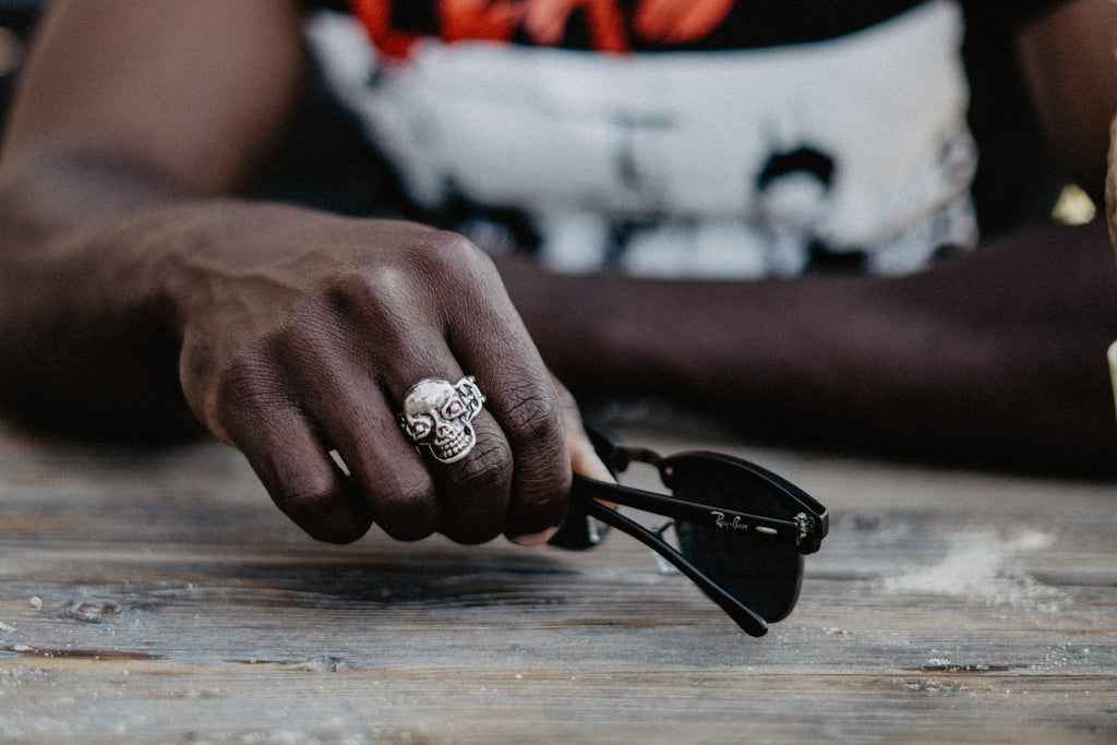 black man wearing a skull ring holding his Ray Ban shades