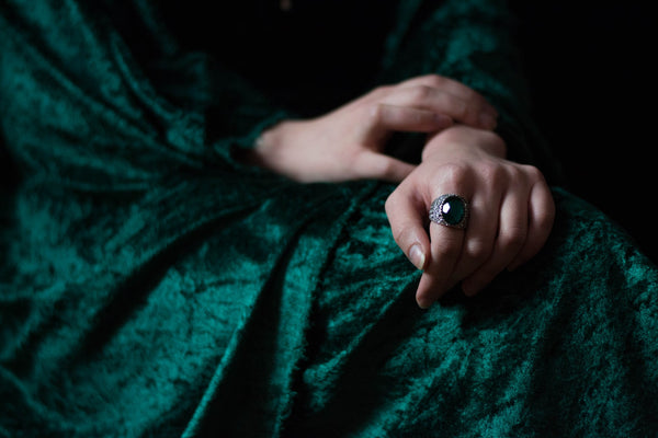 woman's hand wearing an emerald green crystal cocktail ring and green velvet dress