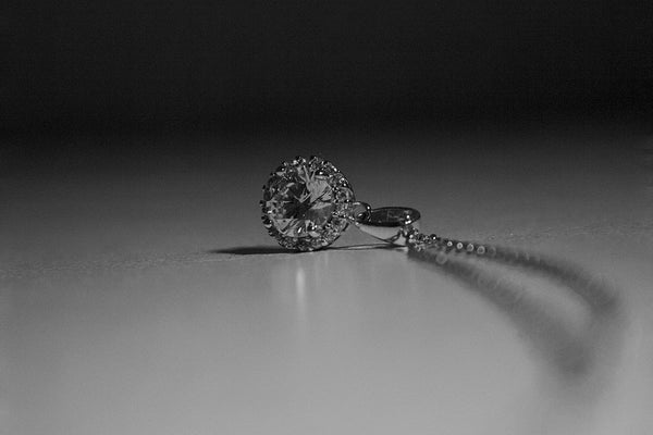 selective focus photograph of a silver pendant necklace on a sleek white surface with dark background