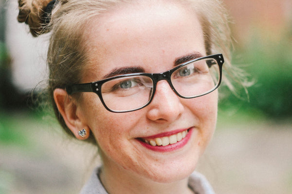 smiling blonde woman in a bun wearing glasses and heart stud earrings