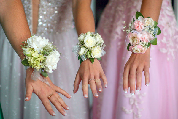three young ladies wearing flower bracelets and fashion rings and prom dresses