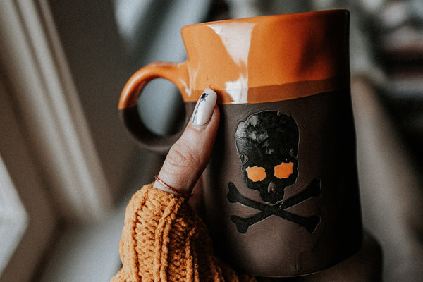 woman in an orange sweater wearing a coffee plated ring holding a halloween themed mug