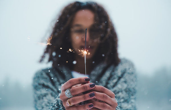 woman wearing an ice blue crystal fashion ring and gold ring with purple nail polish holding up sparkles out in the snow