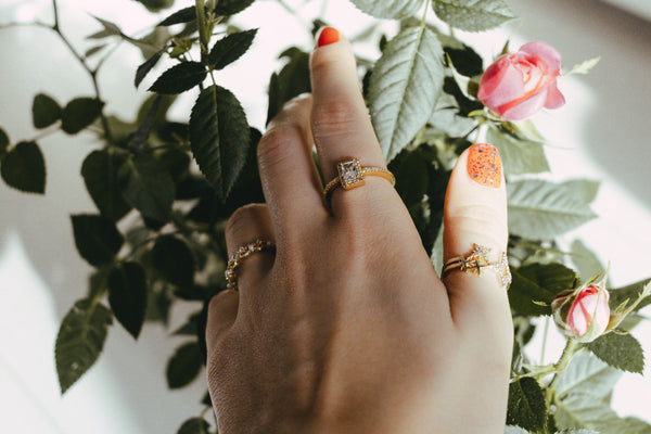 woman with red nails wearing gold-plated fashion rings touching a rose plant
