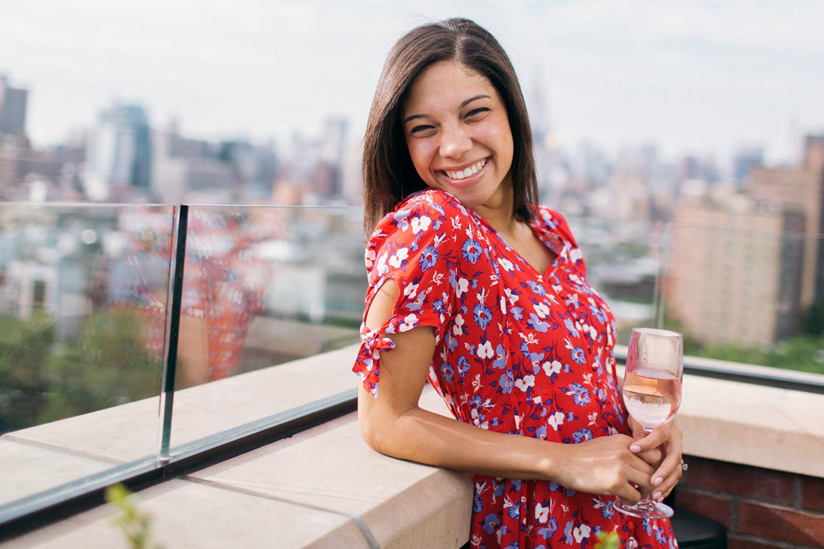 Smiling woman on the rooftop wearing a red floral dress and holding a glass of wine