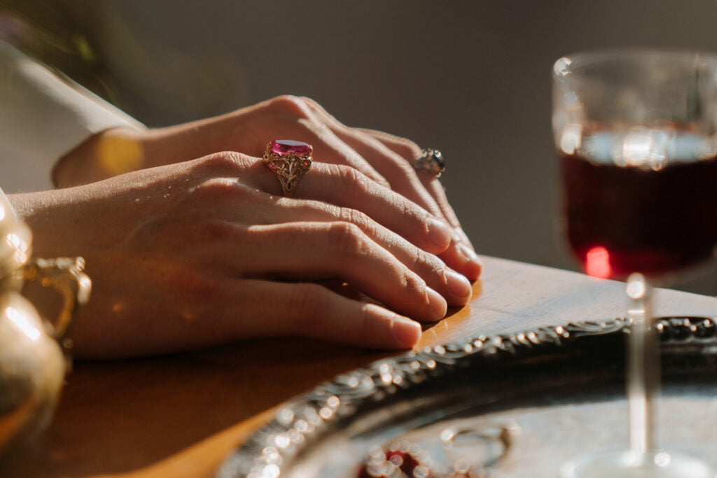 hand wearing ruby cz ring  with glass of wine on table