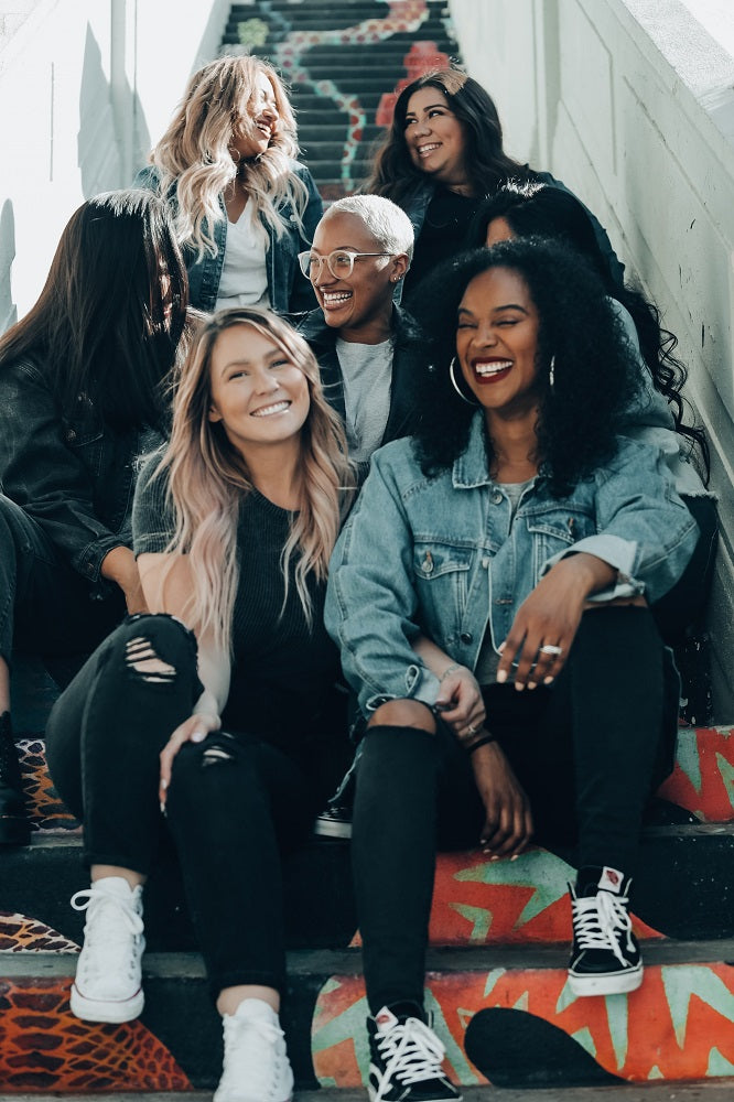 seven smiling women of different ethnicities sitting on steps of stairs
