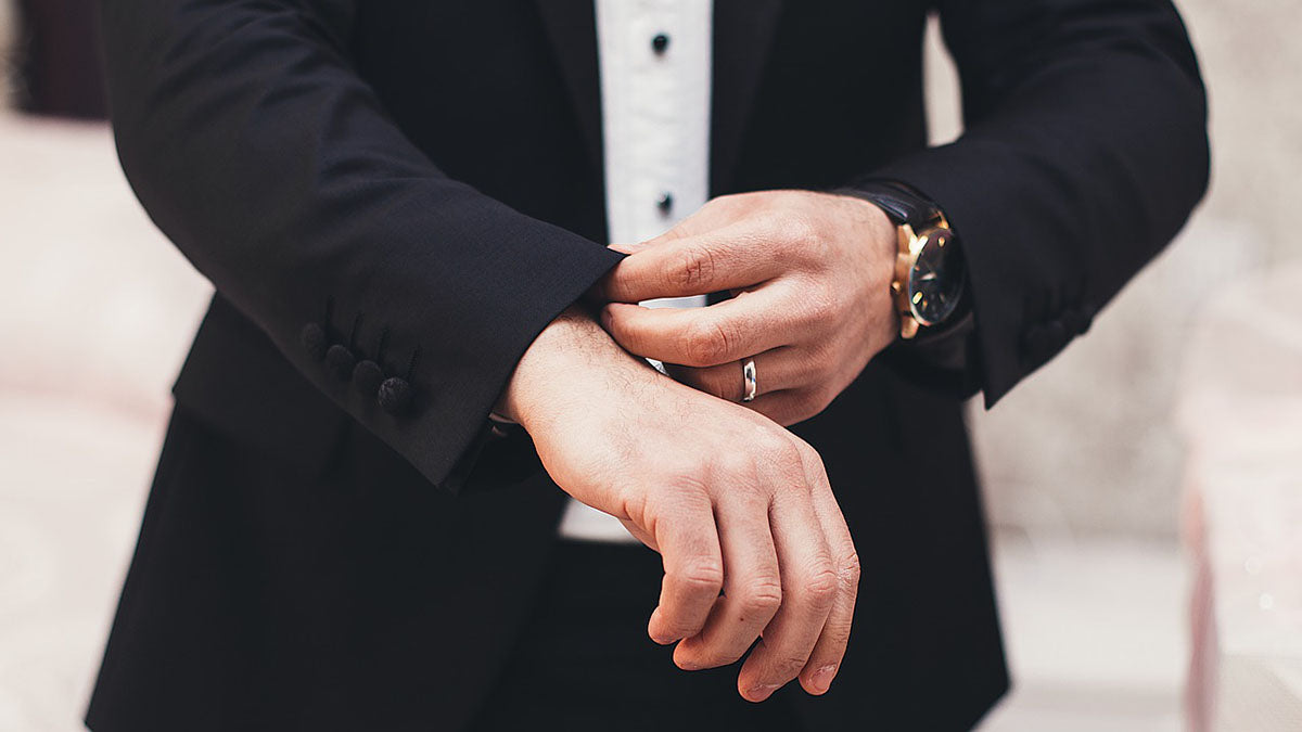 Man in a black suit wearing a ring fixing his sleeve