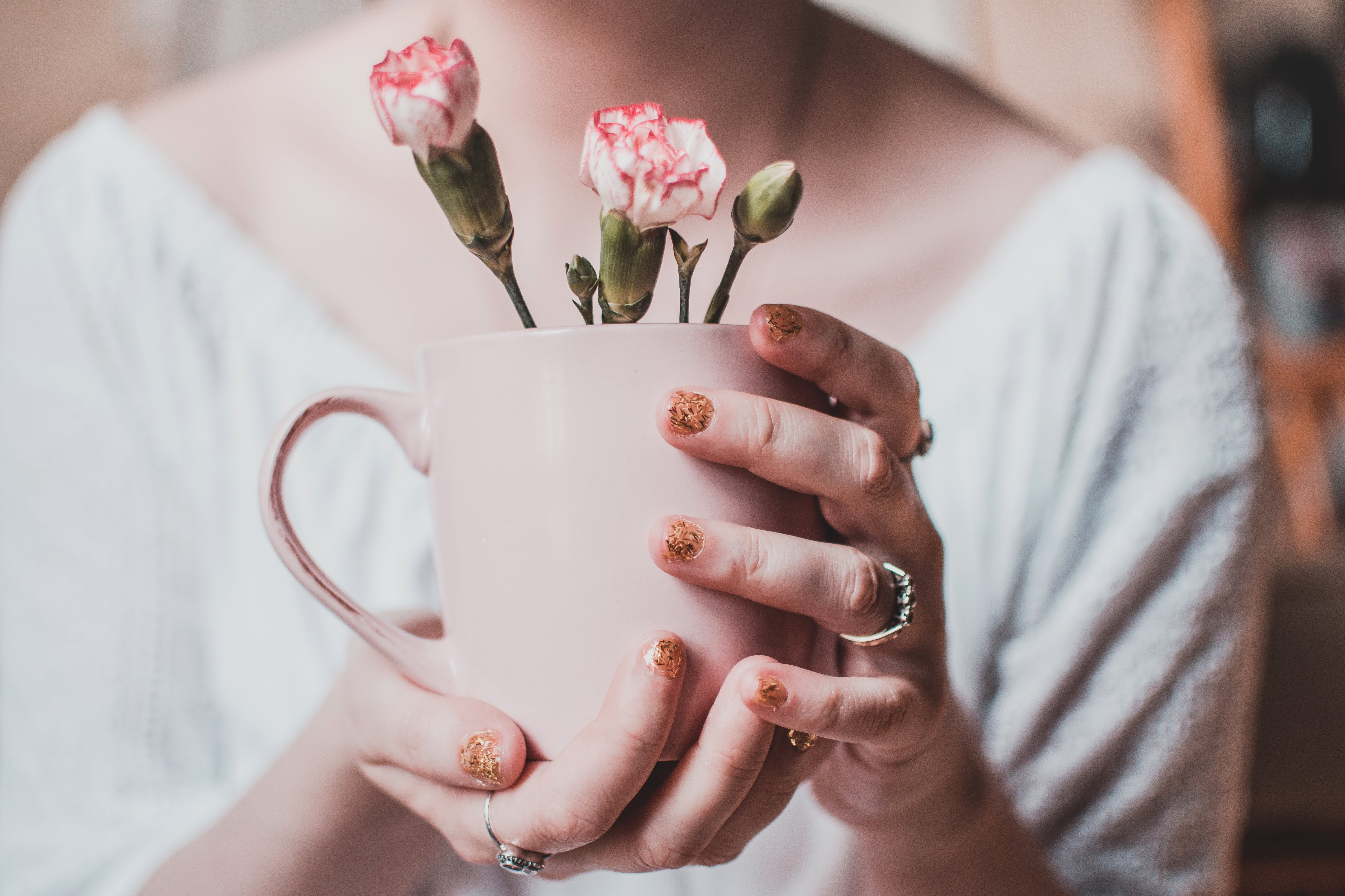 woman with glittery nail polish and stainless steel ring holding a mug with flowers