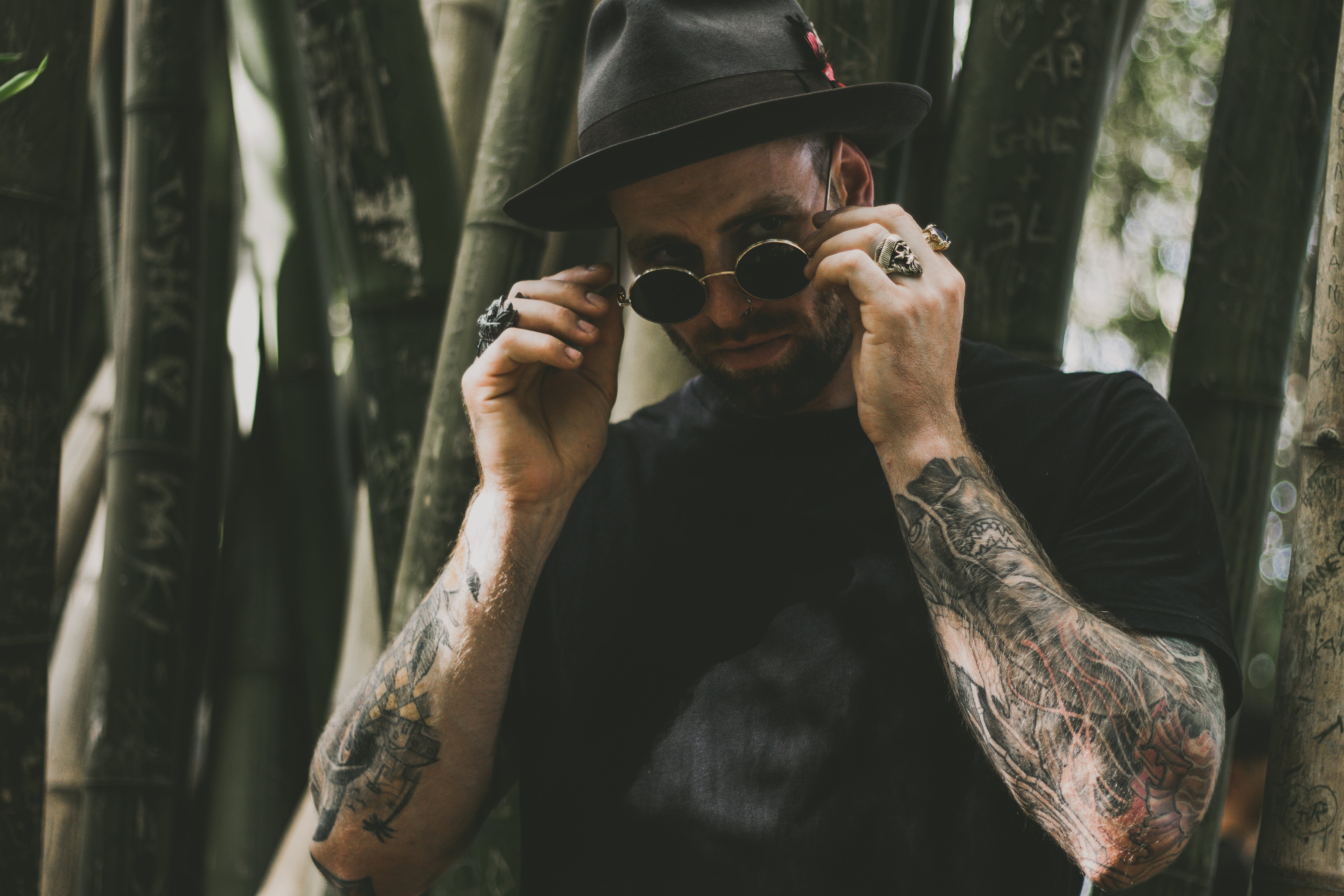 tattooed man wearing a black hat, sunglasses, and biker rings