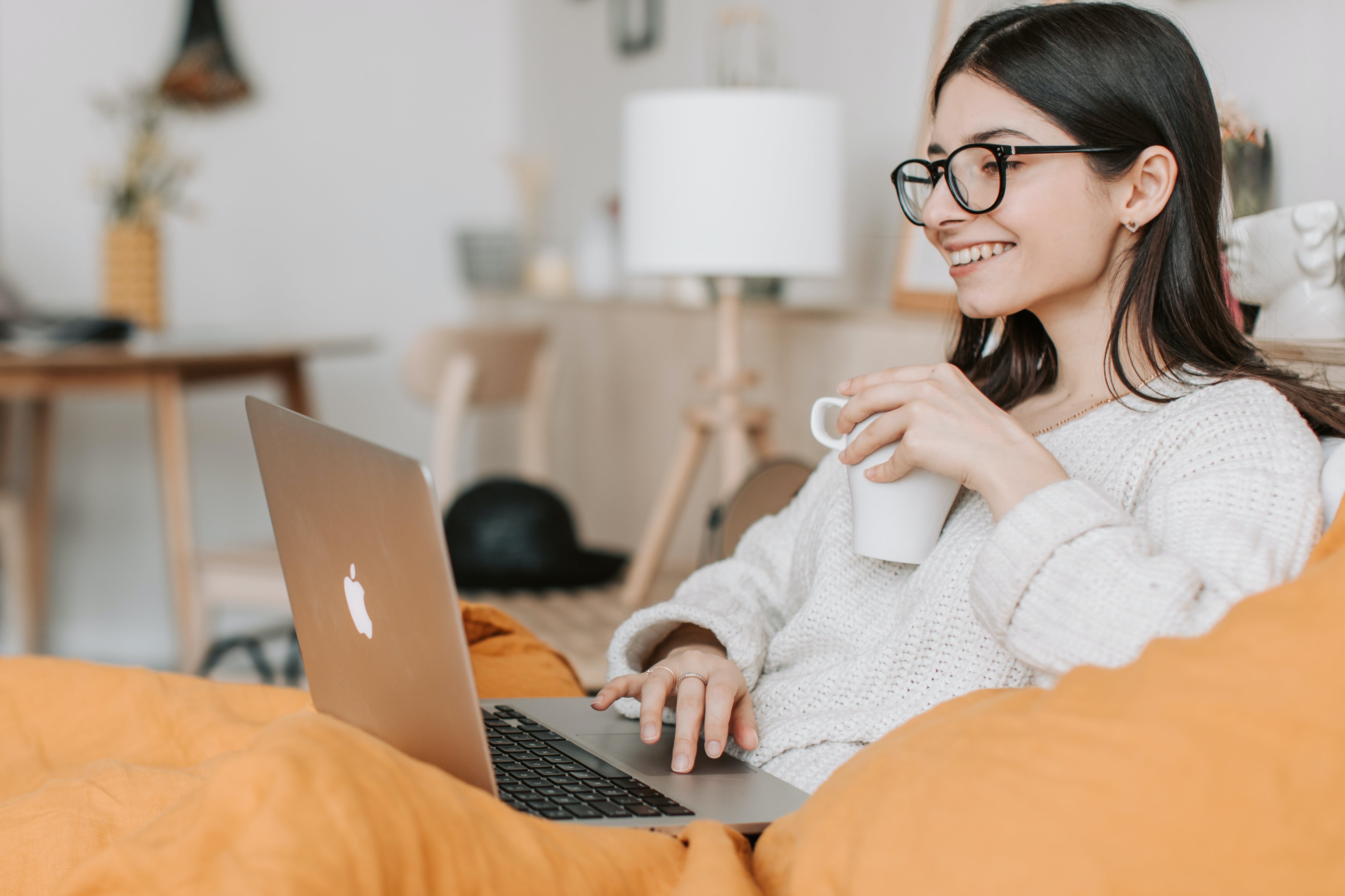 smiling woman wearing glasses holding a cup of coffee and a laptop