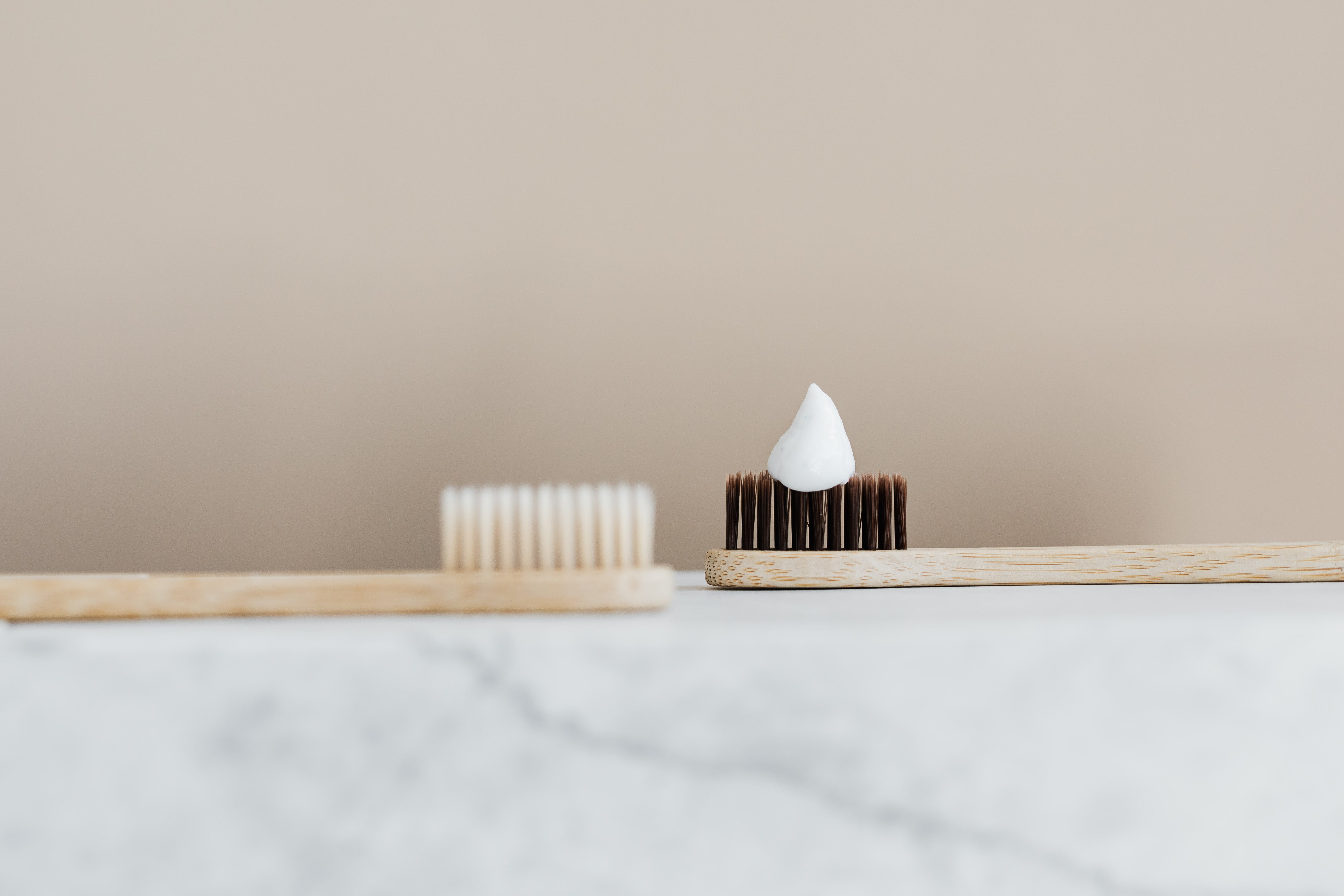 bamboo toothbrush with white bristles and bamboo toothbrush with toothpaste on dark brown bristles