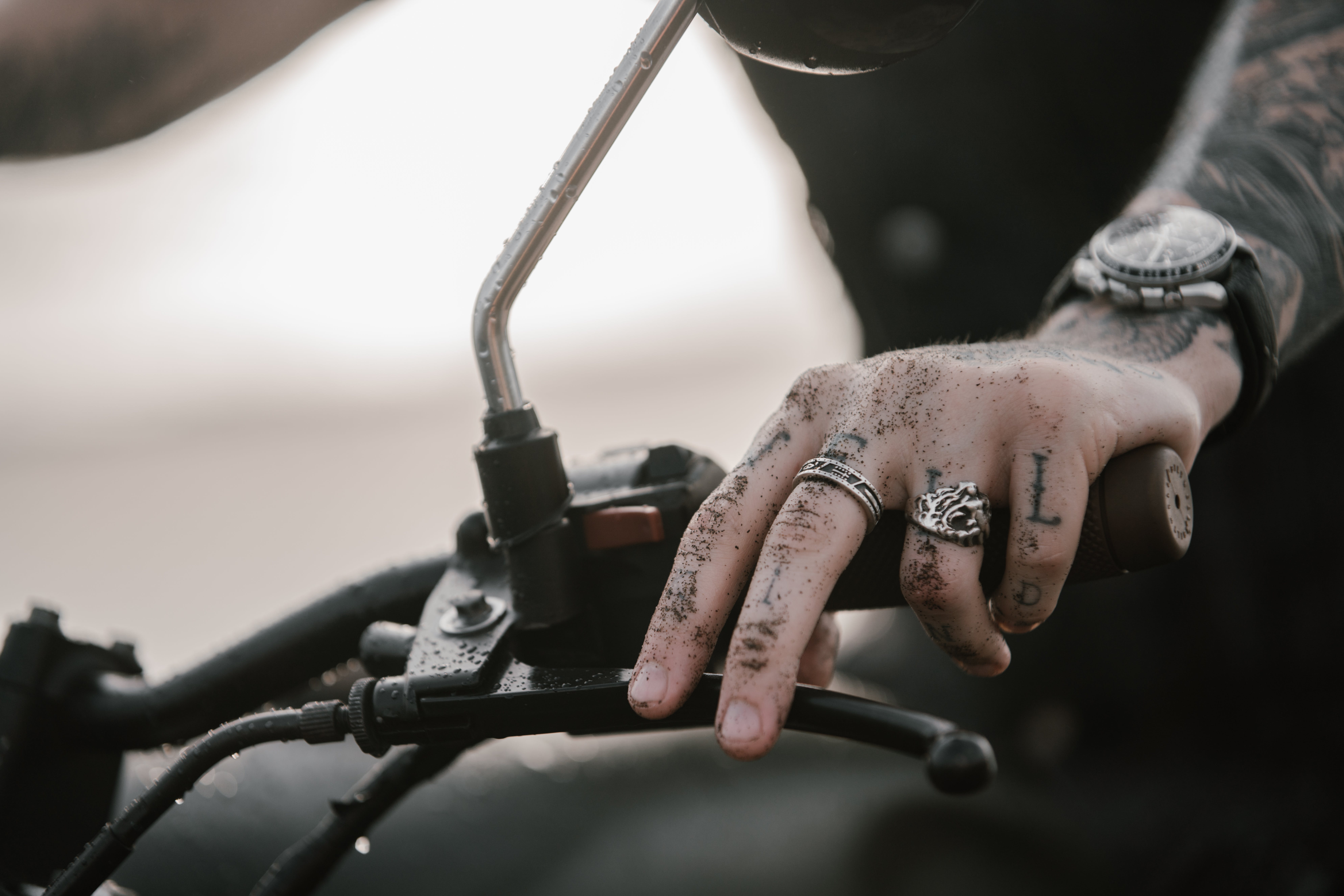 dirty hand of a man wearing stainless steel rings on a motorcycle handle