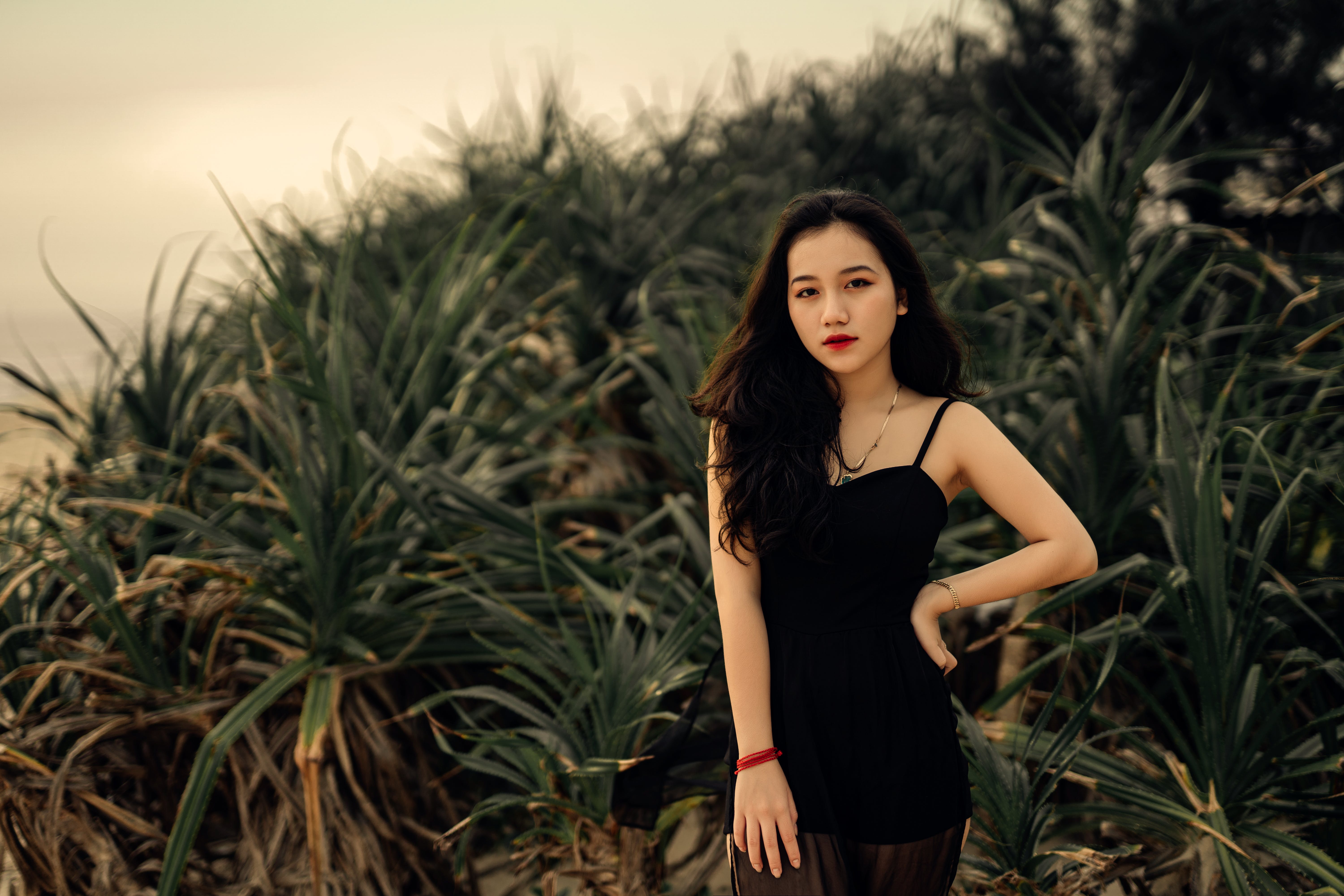 Asian woman in a little black dress wearing fashion jewelry pieces, standing among plants