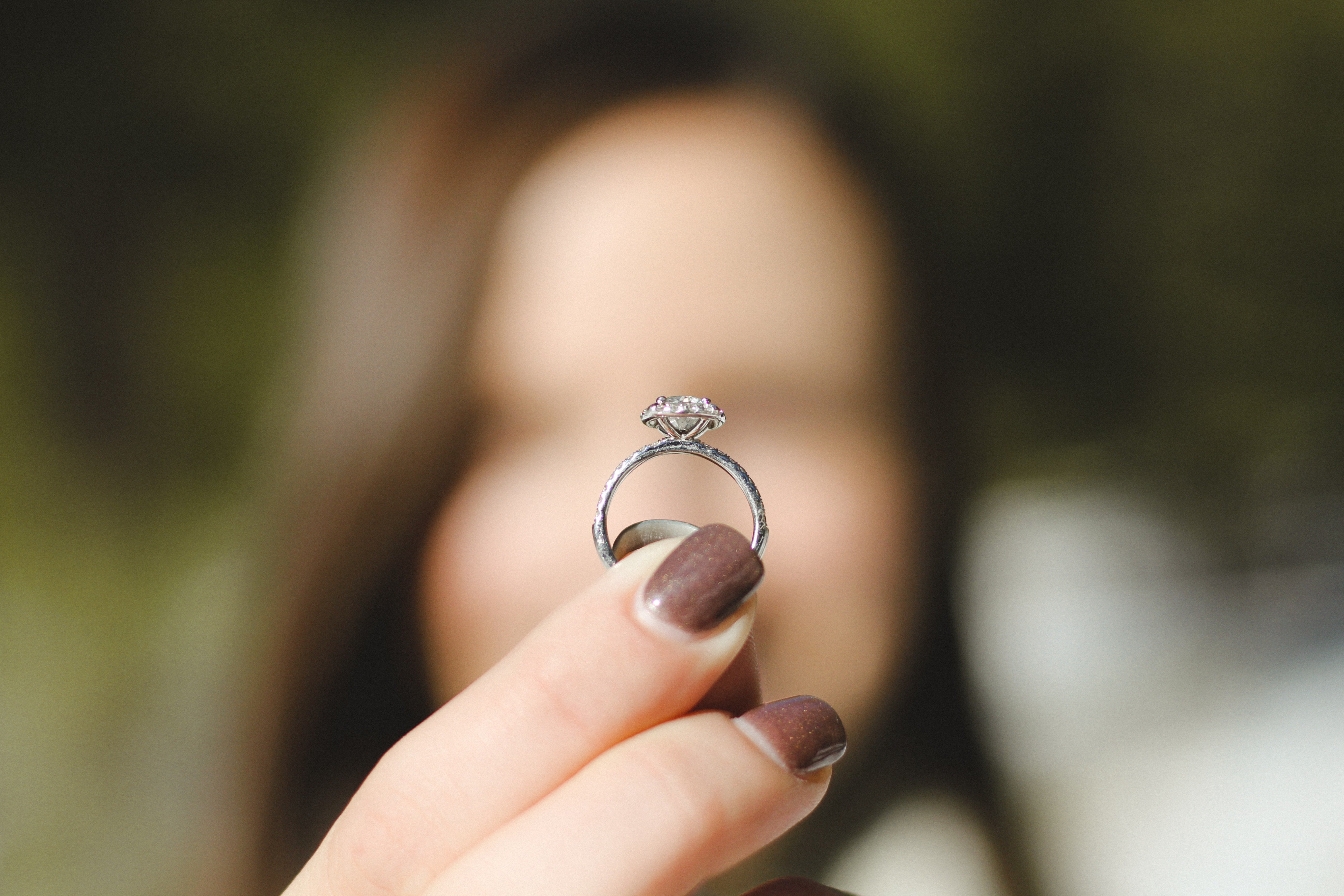 macro shot of a Moissanite engagement ring held by a woman with mocha-colored nails