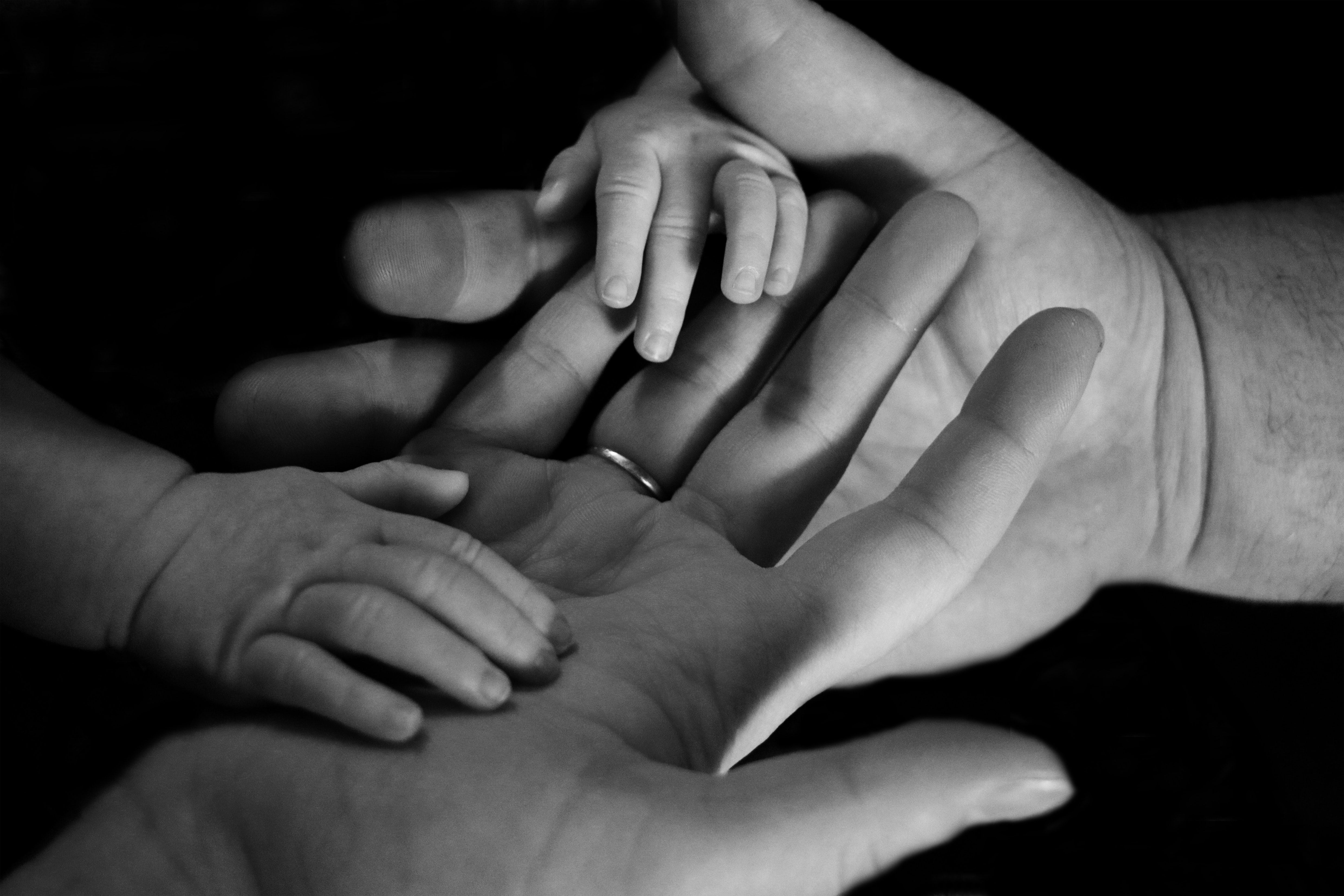 black and white photo of dad's hands wearing a ring holding a baby's hands