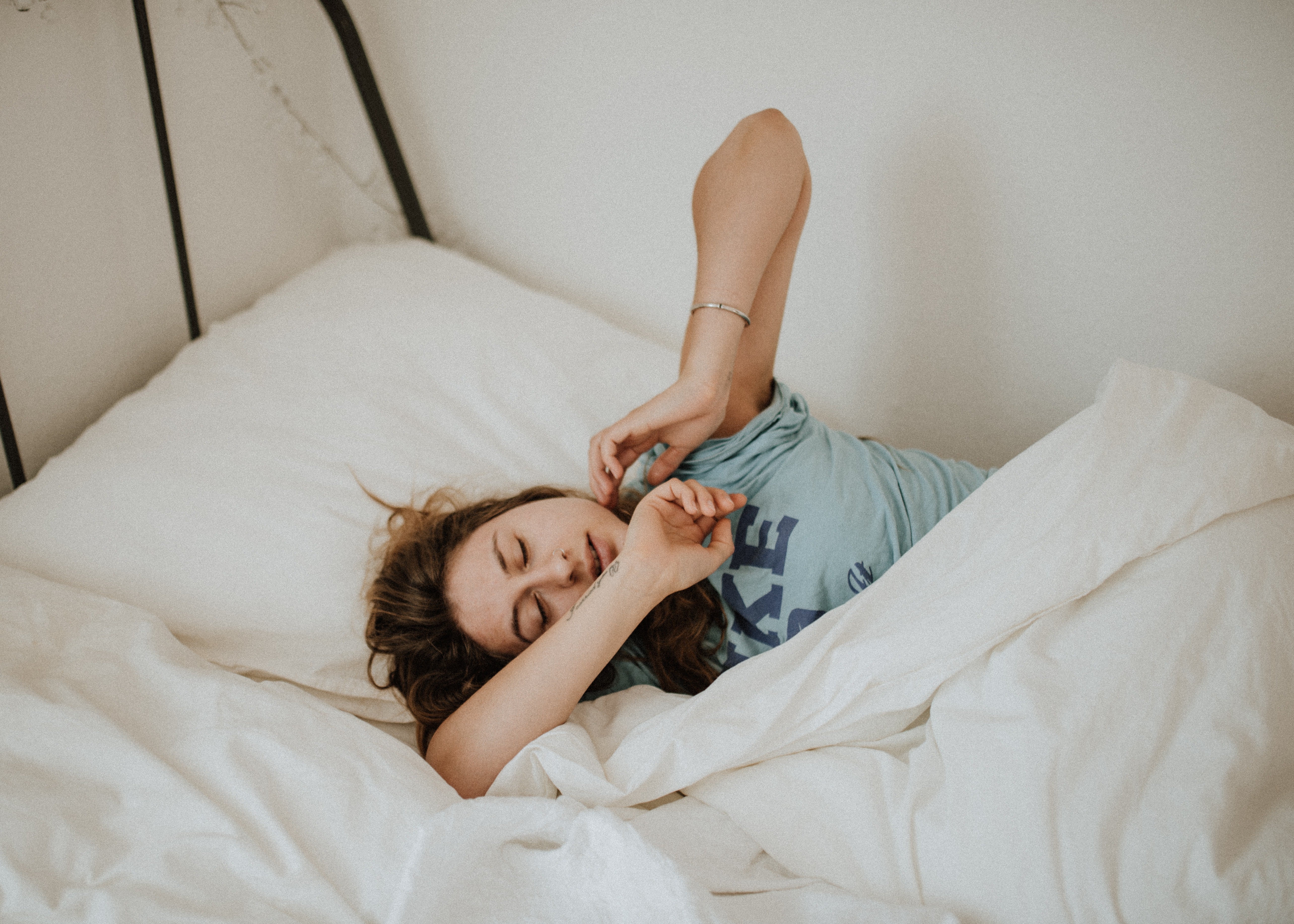 woman in a light blue shirt sleeping in a bed with white sheets