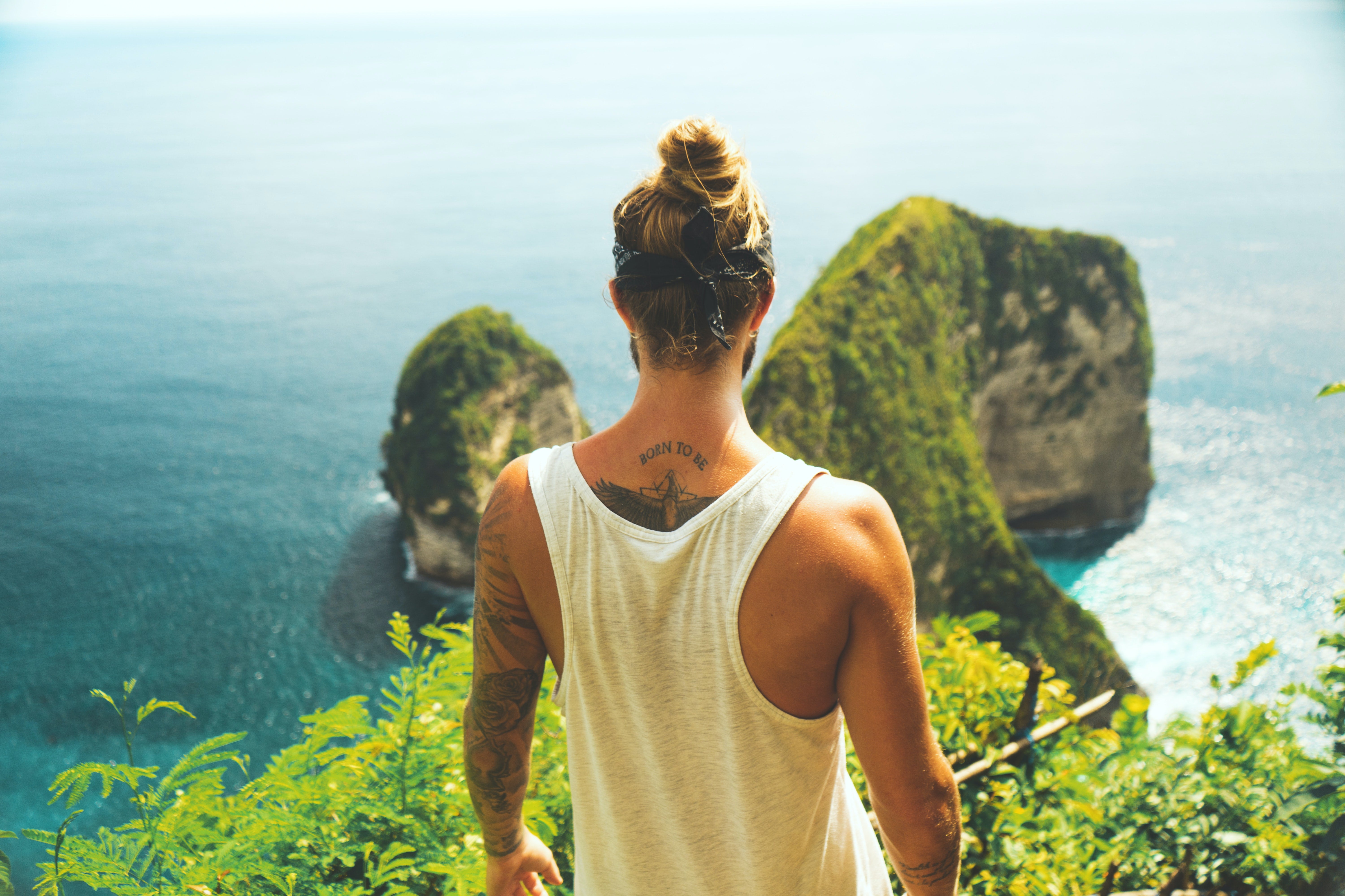man with a man bun wearing a sleeveless shirt looking over the ocean on a cliff