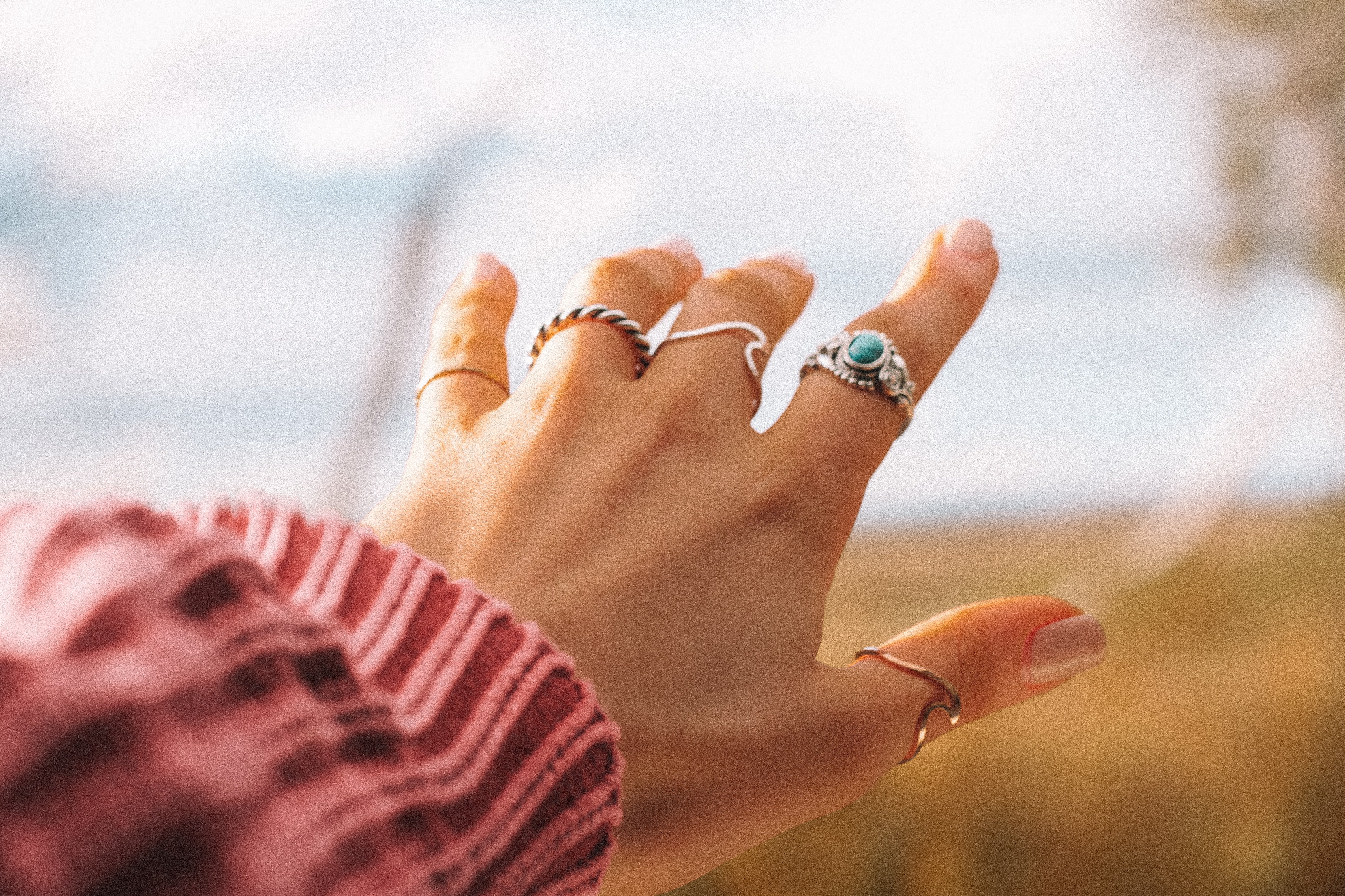 hand of woman wearing old rose sweater and silver rings in all fingers
