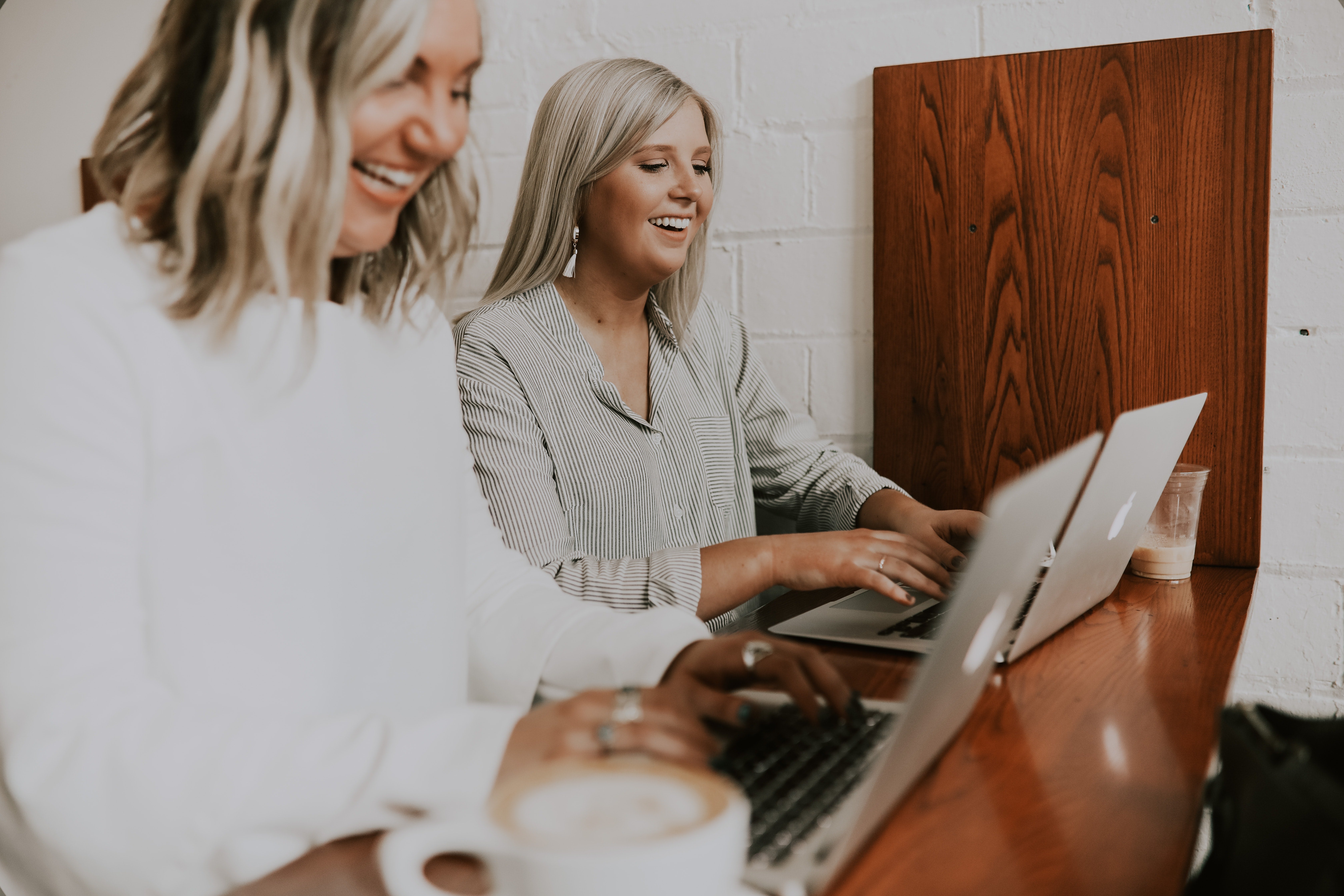 two blonde women smiling while working in front of their laptops