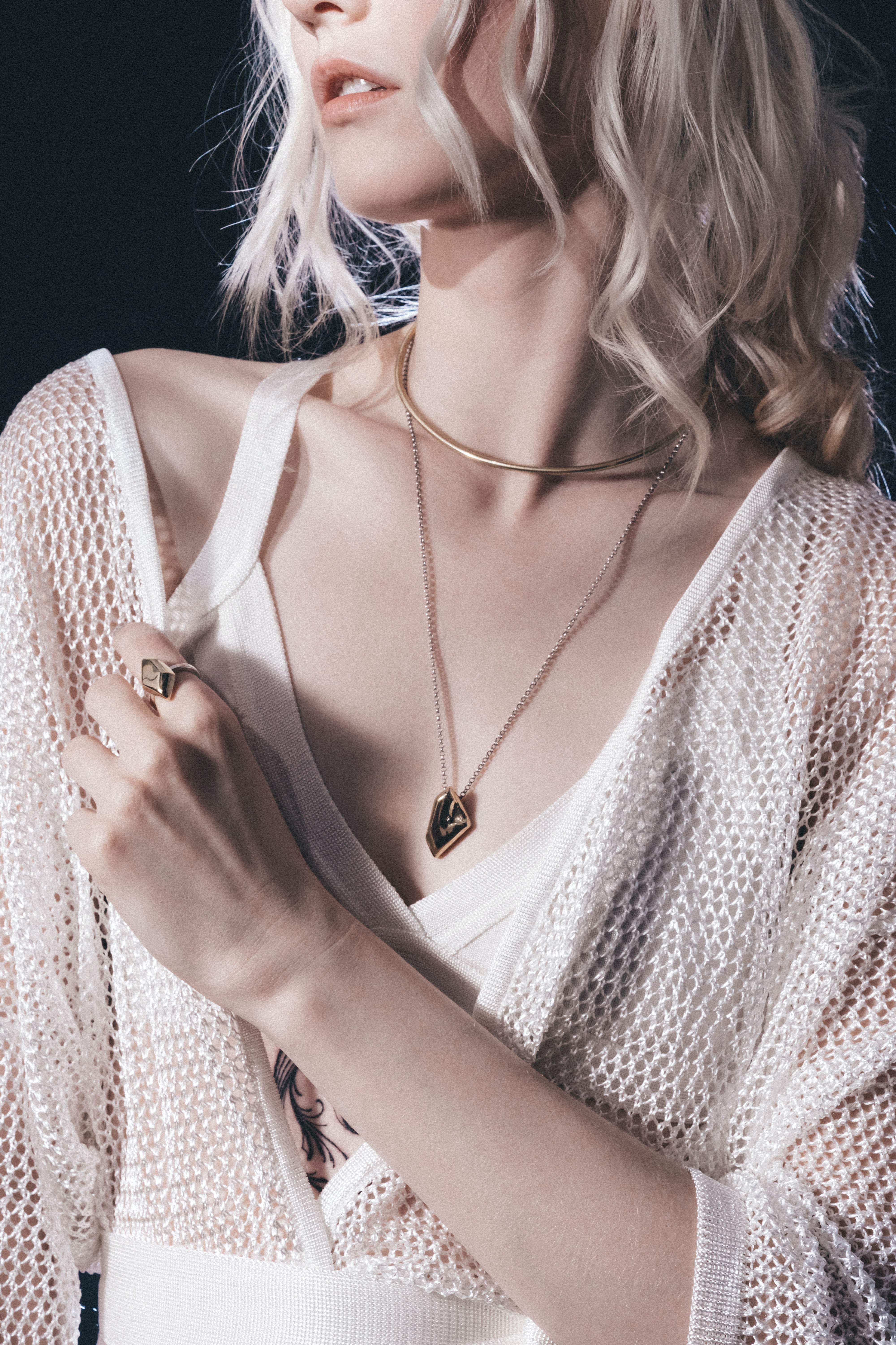 blonde woman wearing gold fashion jewelry which includes a choker, a pendant necklace, and a statement ring