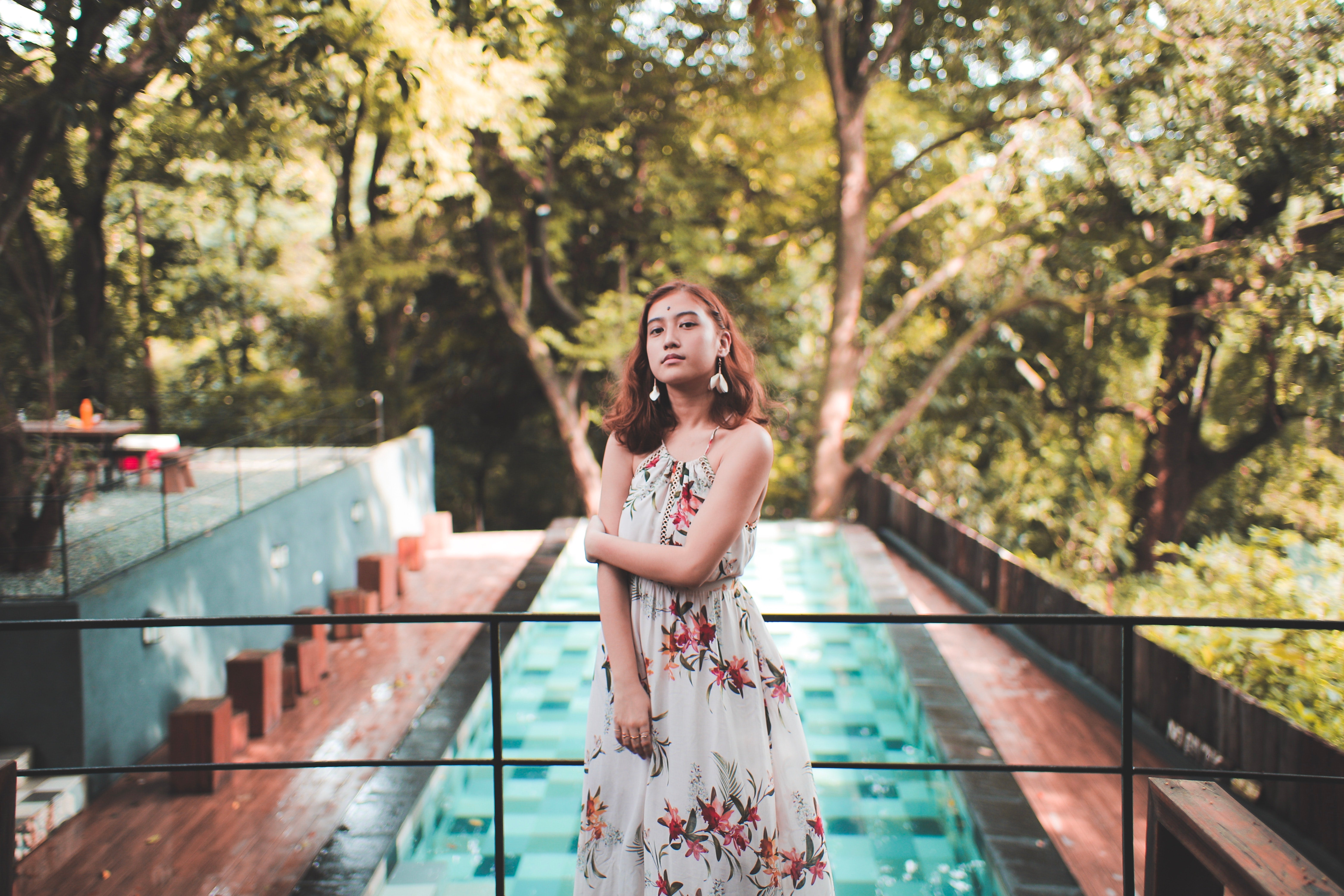 woman in a floral dress wearing statement earrings with a swimming pool in the background