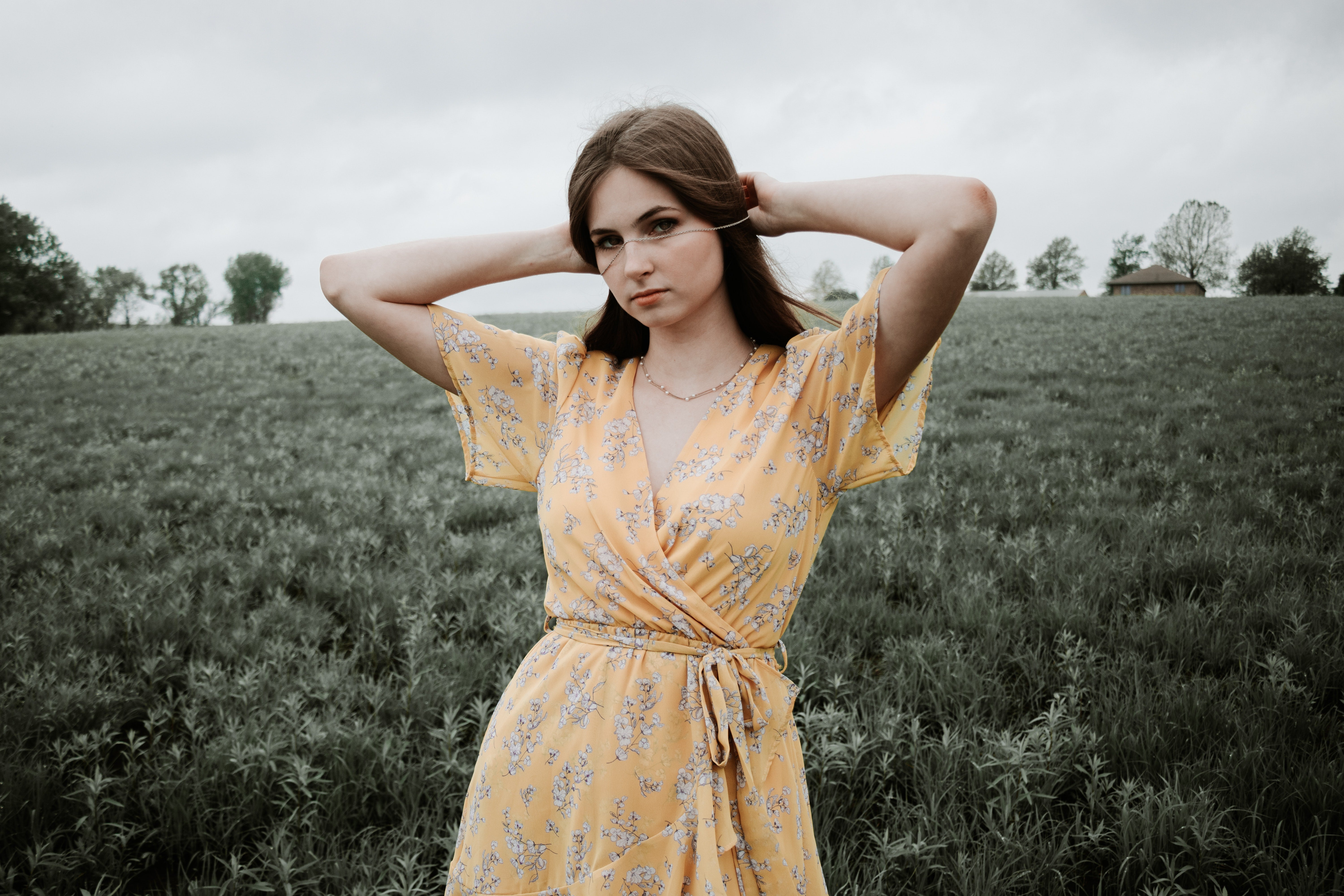 woman in yellow floral dress and gold necklace standing on green grass field during daytime