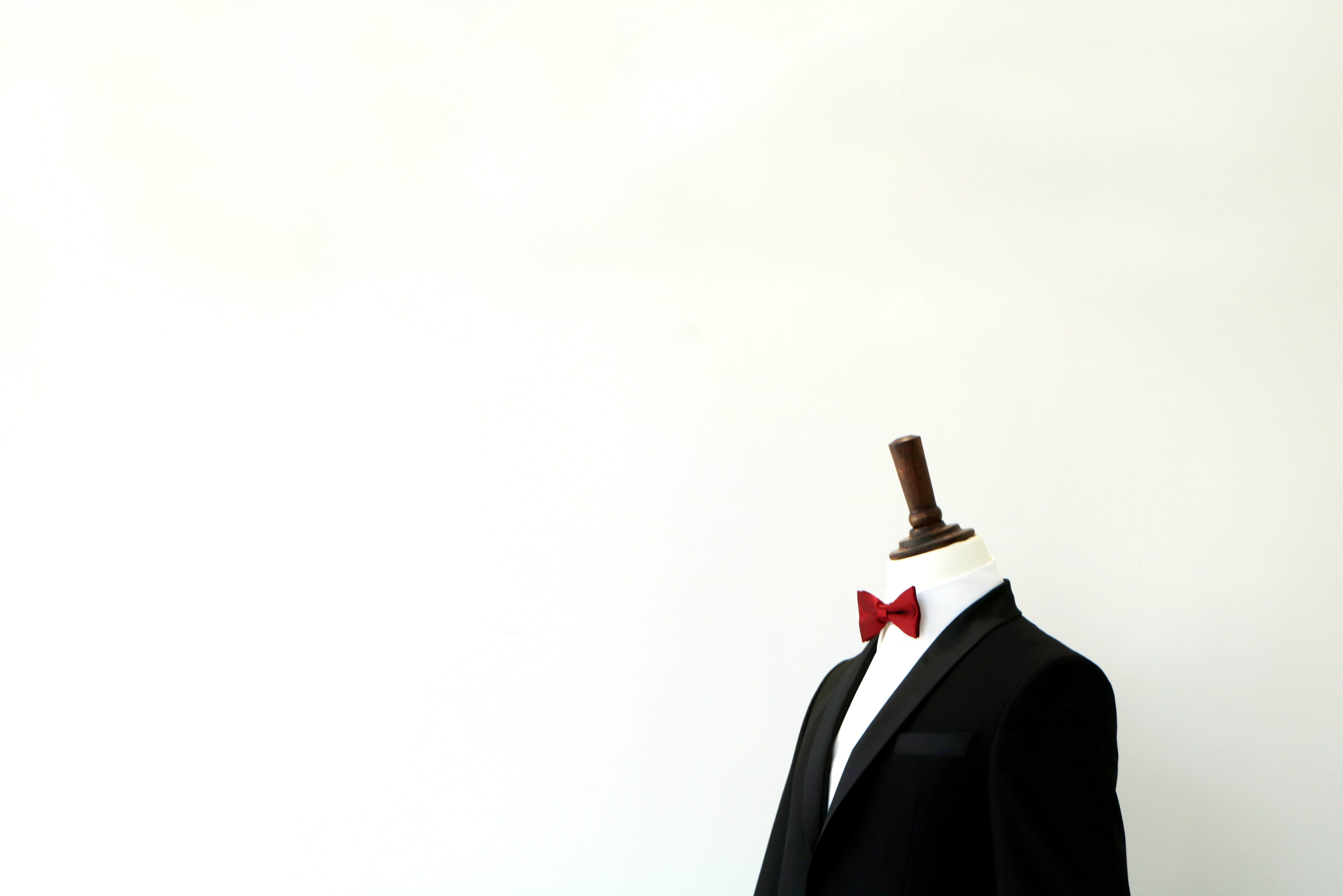 headless mannequin wearing a black suit and red bow tie against a white wall