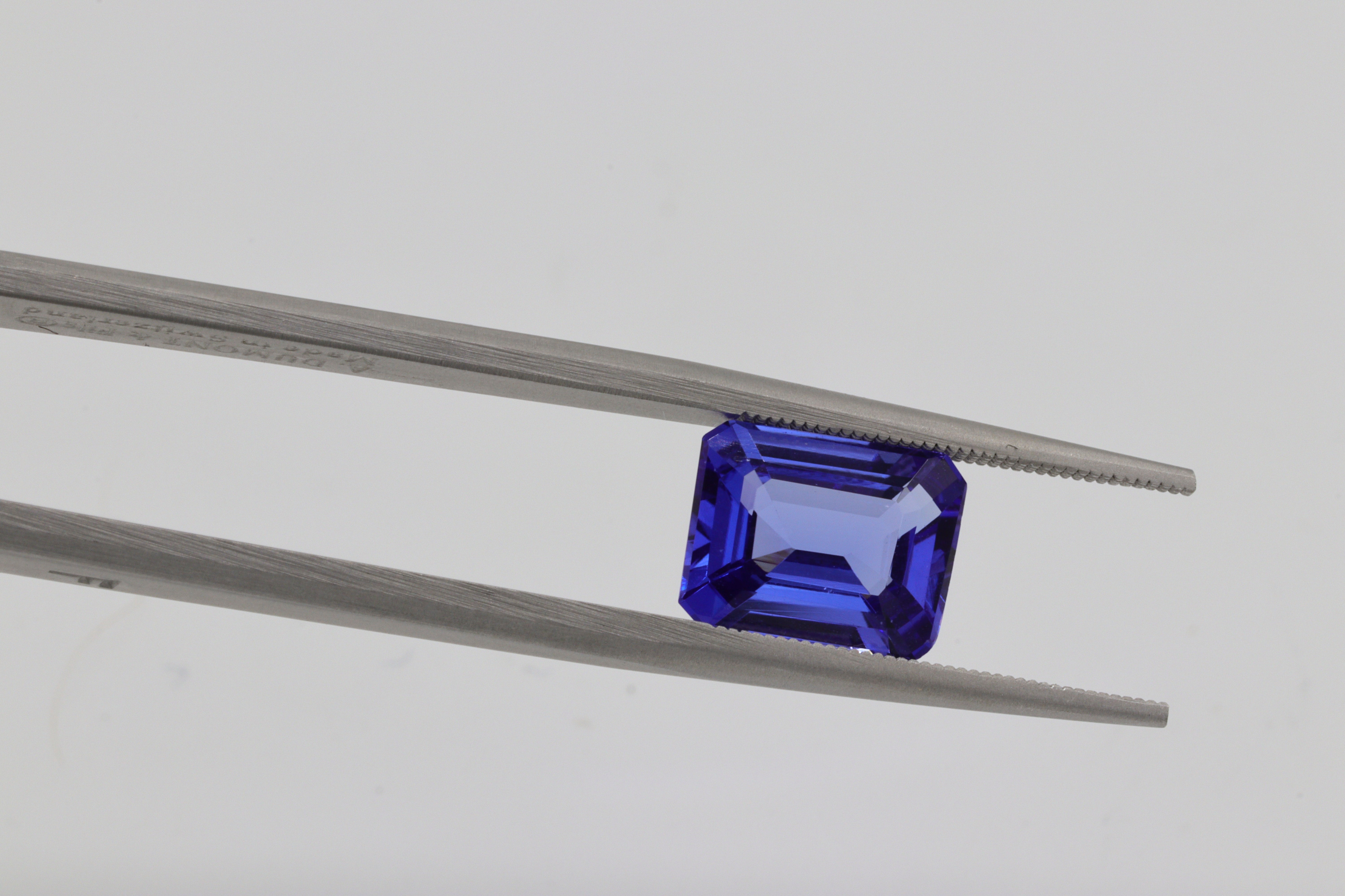 Emerald-cut tanzanite gemstone held by a long nose tool