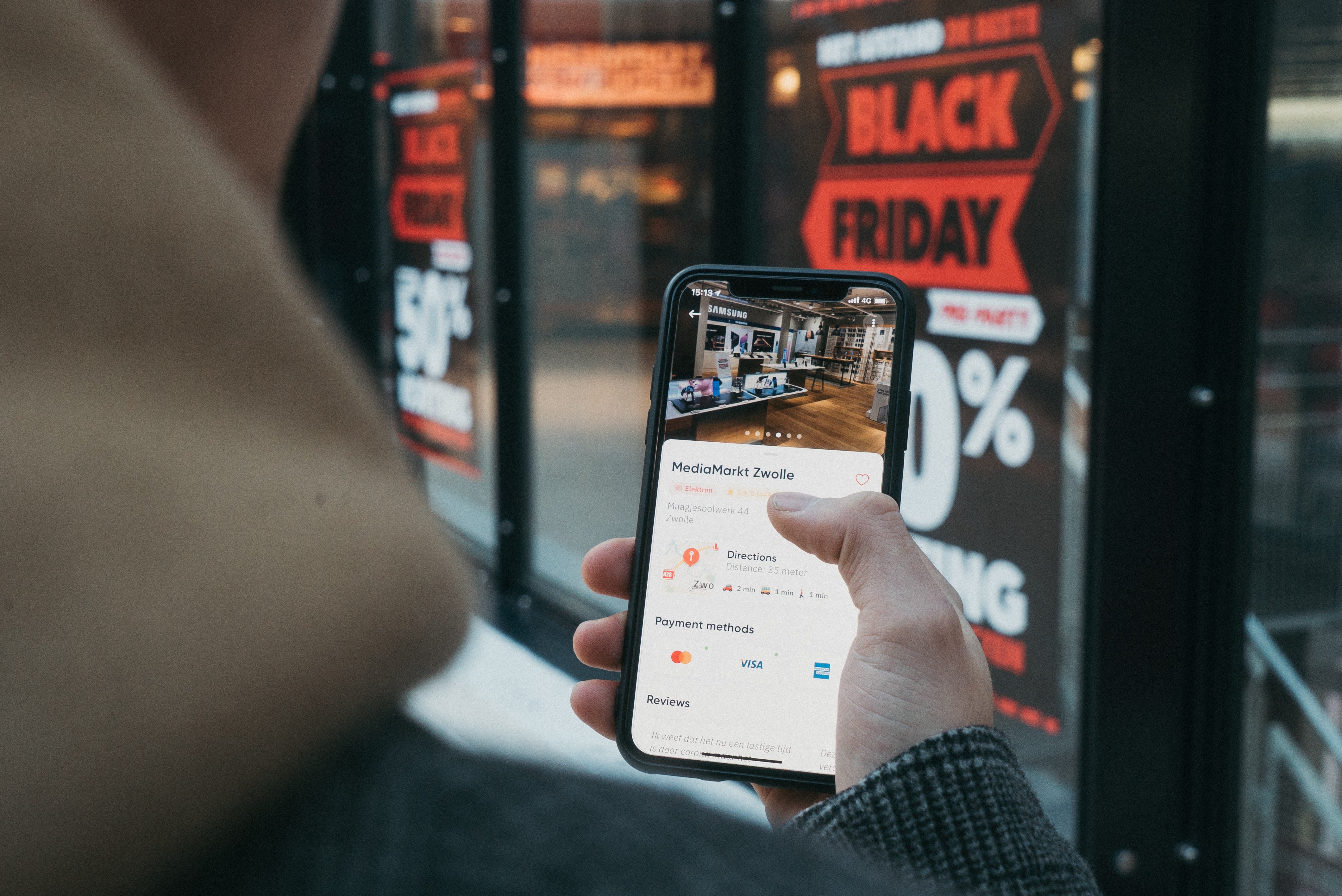person holding out mobile phone with a shop window in the background with Black Friday sale poster