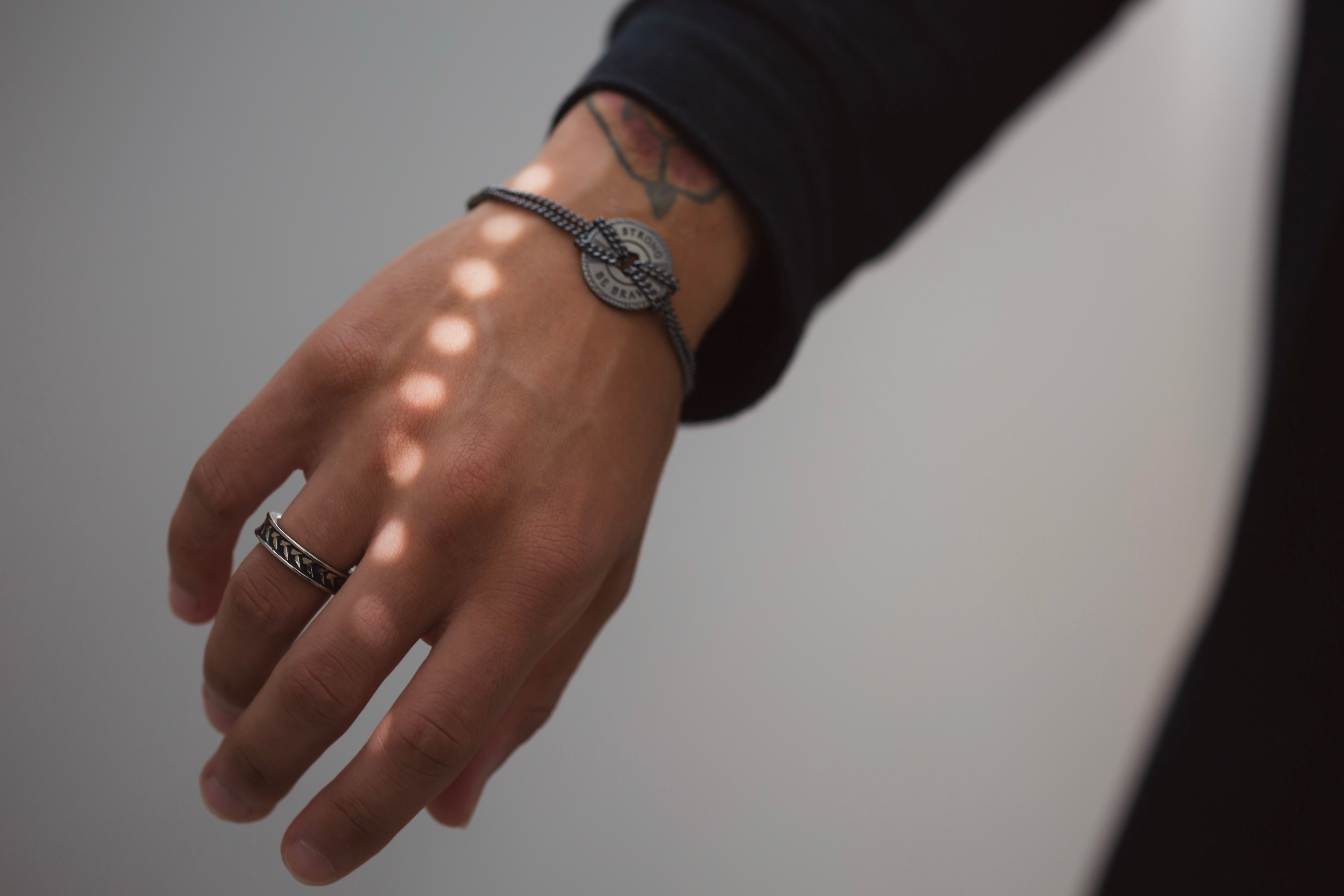 man's hand with stainless steel ring on ring finger and a bohemian-style bracelet on wrist