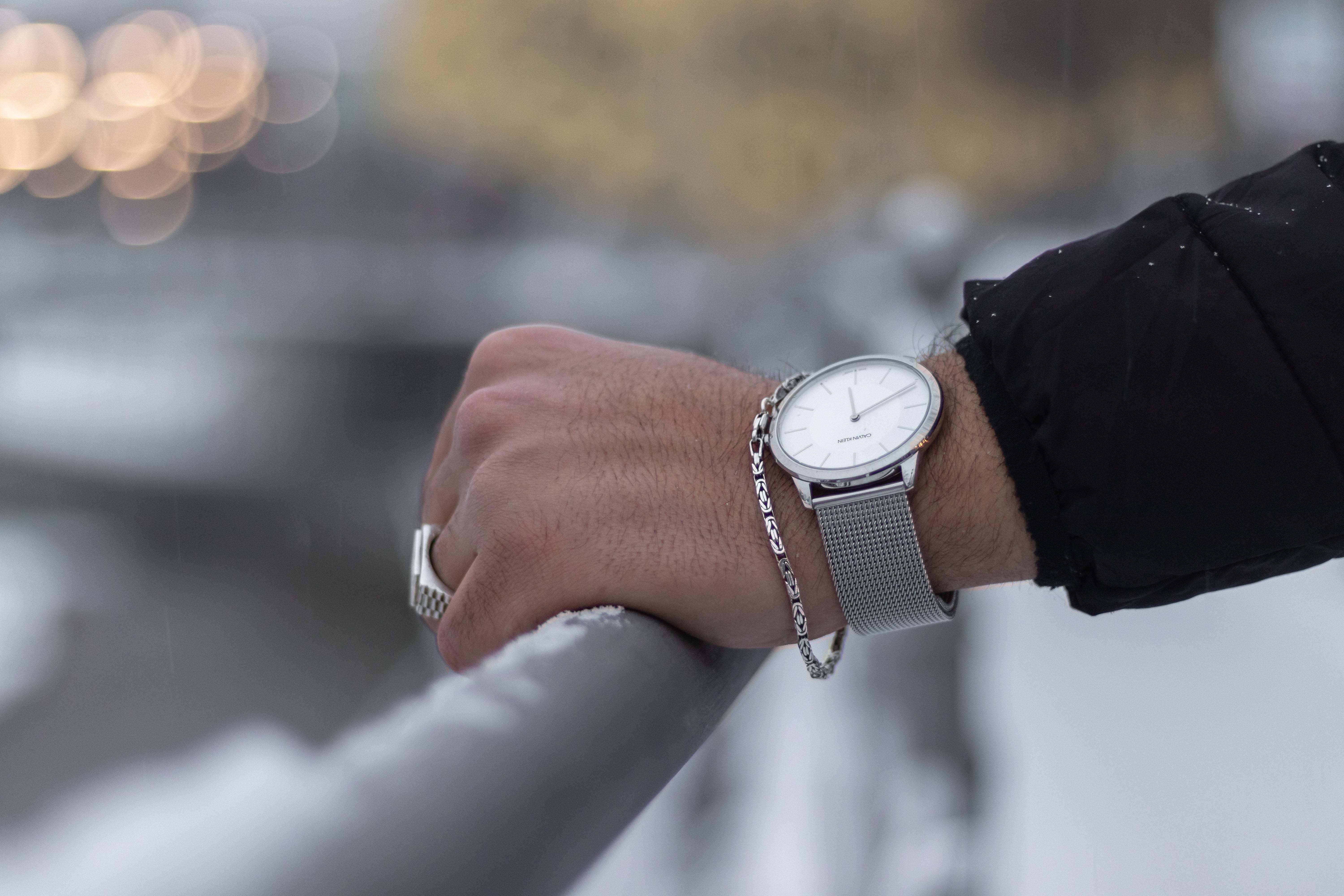 man's hand with stainless steel ring, thin bracelet, and watch, holding on a railing