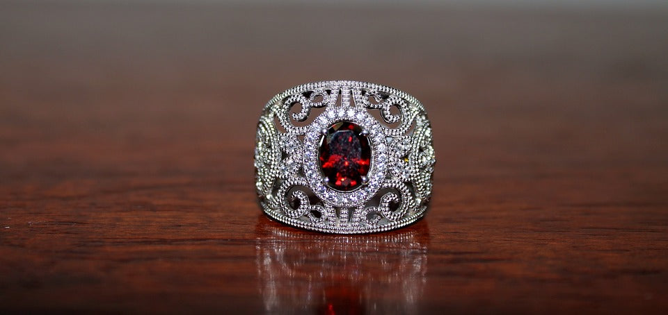 ornate stainless steel ring with an oblong garnet center stone on a wooden surface