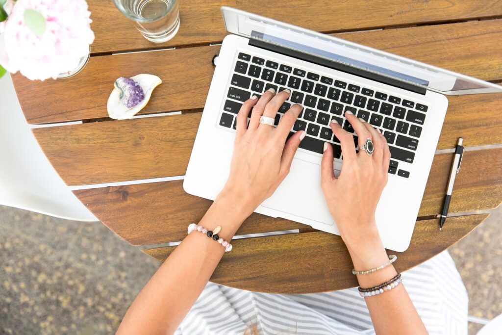 woman wearing fashion rings and bracelets typing on a silver laptop on a wooden table