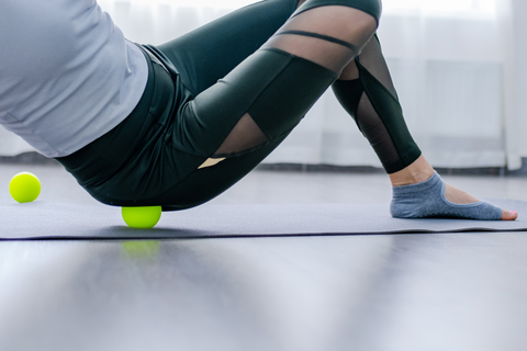 fit woman using massage ball on hip while sitting on yoga mat