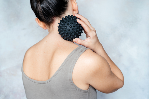 woman using black spiky massage ball on neck