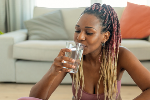 african american woman drinking a glass of water while sitting on the floor