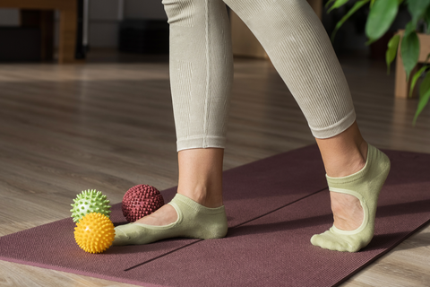 woman standing on yoga mat with spiky massage balls of different colors